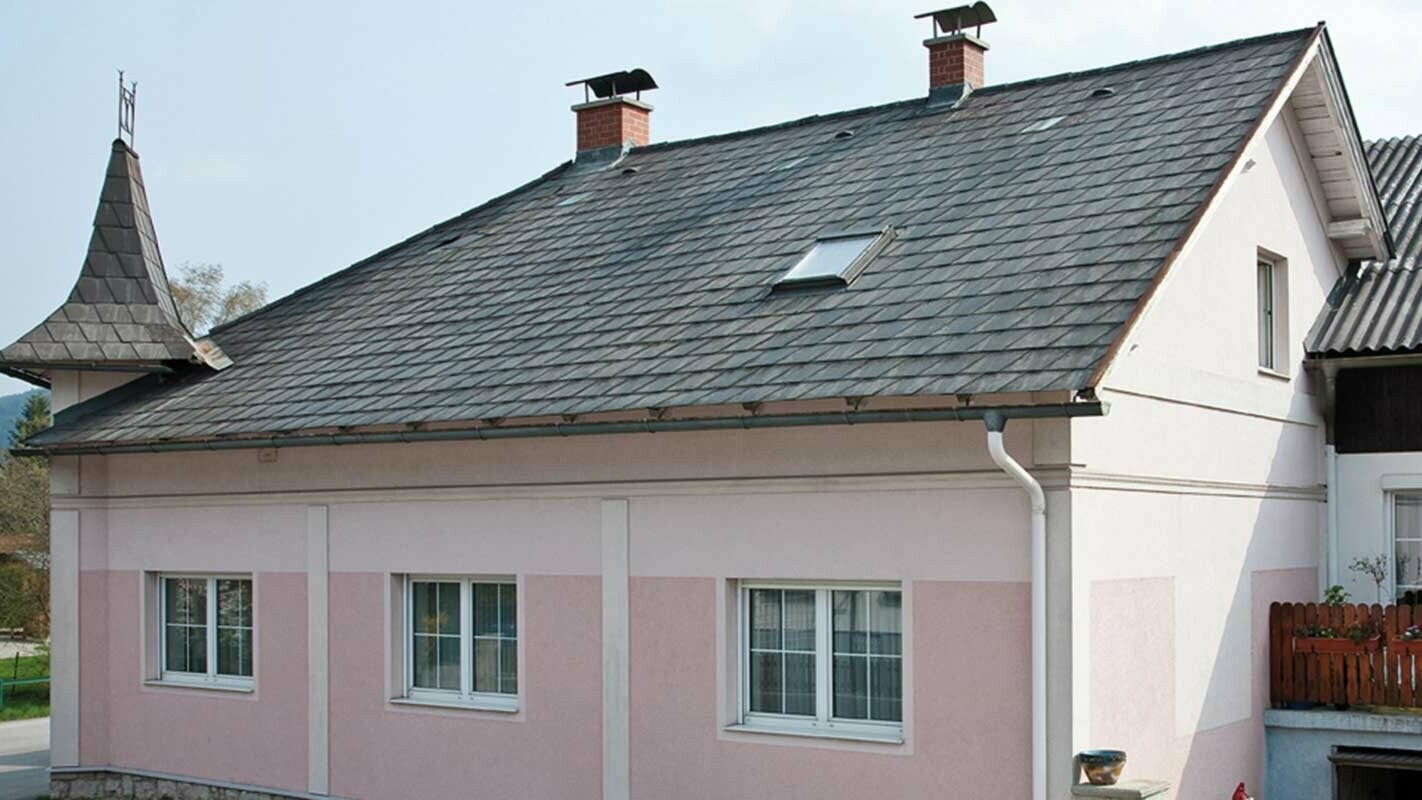 Dům v Rakousku s věžičkami a růžovou fasádou před sanací střechy za použití PREFA falcovaných střešních tašek - původně osinkocementová krytina Eternit 