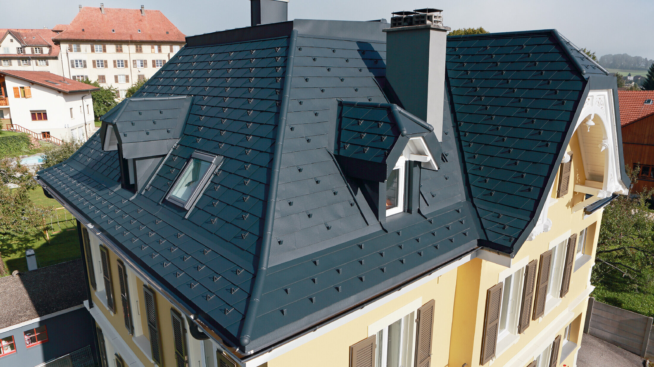 Vila ve Švýcarsku, s mnoha úžlabími a malými vikýři ve střeše; střecha je pokrytá hliníkovým PREFA falcovaným šindelem v barvě P.10 antracitové