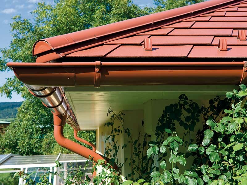 Detail PREFA falcovaného střešního šindele v cihlově červené barvě se žlabem vhodné barvy.