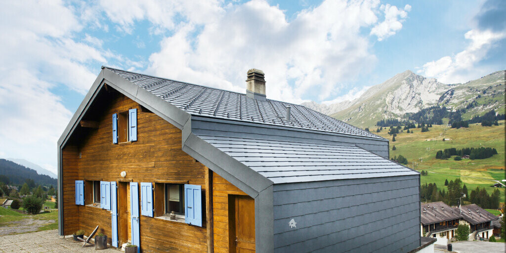 Haus in den Bergen der Schweiz mit Holzfassade kombiniert mit der PREFA Dach- und Wandraute in Steingrau