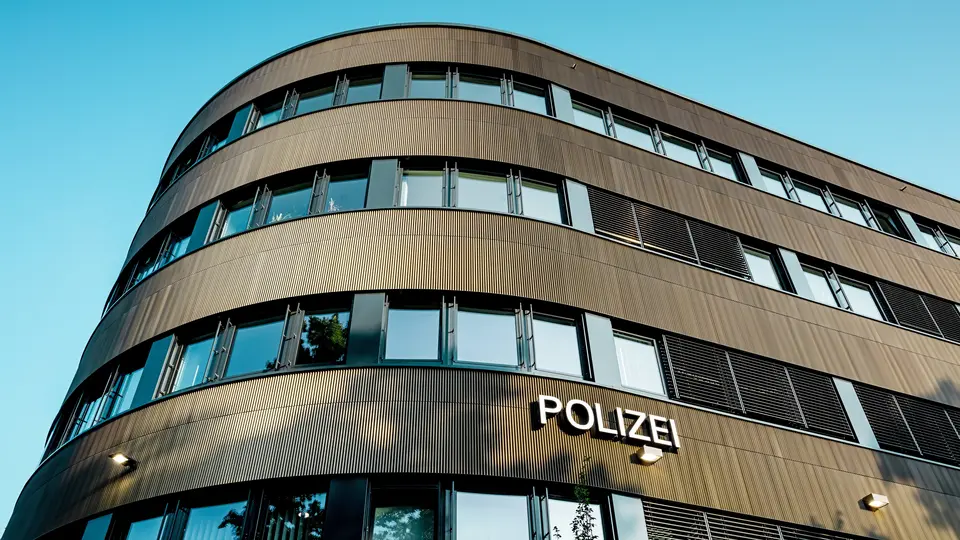 Dramatický pohled zdola na zakřivenou novostavbu policejní stanice 43 v Hamburku: Výrazná hliníková fasáda PREFA z eloxovaných extrudovaných profilů „Zacke“ ve střední bronzové barvě je architektonickým poutačem. Jemná, rytmická struktura vytváří dynamické světelné a stínové vzory a zdůrazňuje plynulé křivky budovy. Hliník PREFA nabízí vysokou odolnost proti povětrnostním vlivům, ochranu proti korozi a dlouhou životnost – udržitelné a nenáročné řešení pro precizní a moderní fasádní architekturu.
