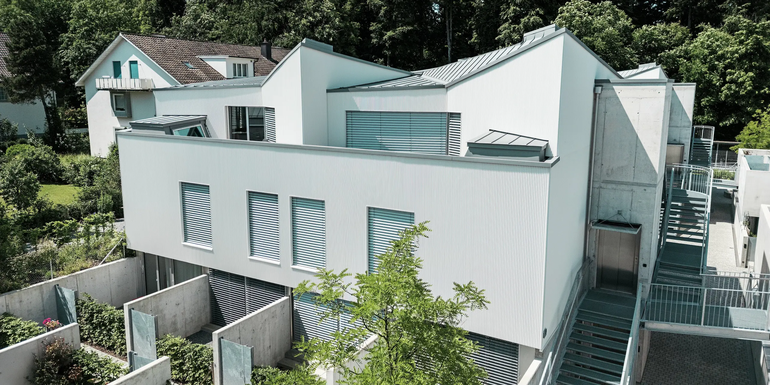 Vogelperspektive auf ein Ensemble moderner Tiny Homes in Zollikerberg mit PREFA Zackenprofil-Fassade in P.10 Reinweiß und PREFALZ Dächern in Patinagrau. Die klaren Linien und kontrastreichen Materialien verleihen dem Projekt eine markante Optik. Hochwertiges Aluminium sorgt für Langlebigkeit, Witterungsschutz und architektonische Präzision auf kleinstem Raum.