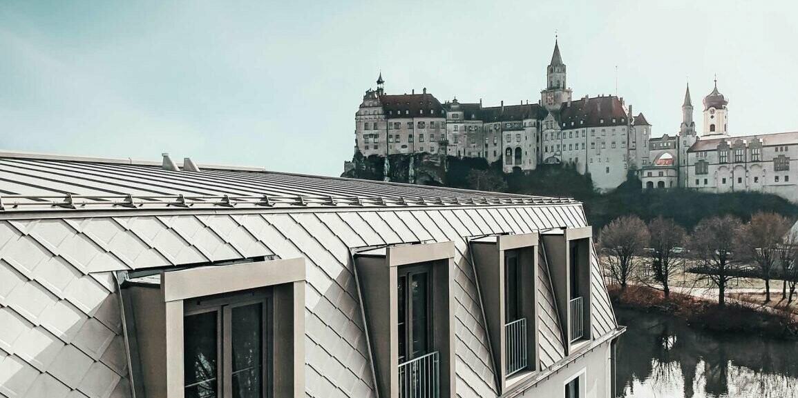 V popředí je vidět bronzově zbarvená střecha PREFA na Karl Hotelu Sigmaringen, v pozadí je vidět přilehlý palác Sigmaringen.