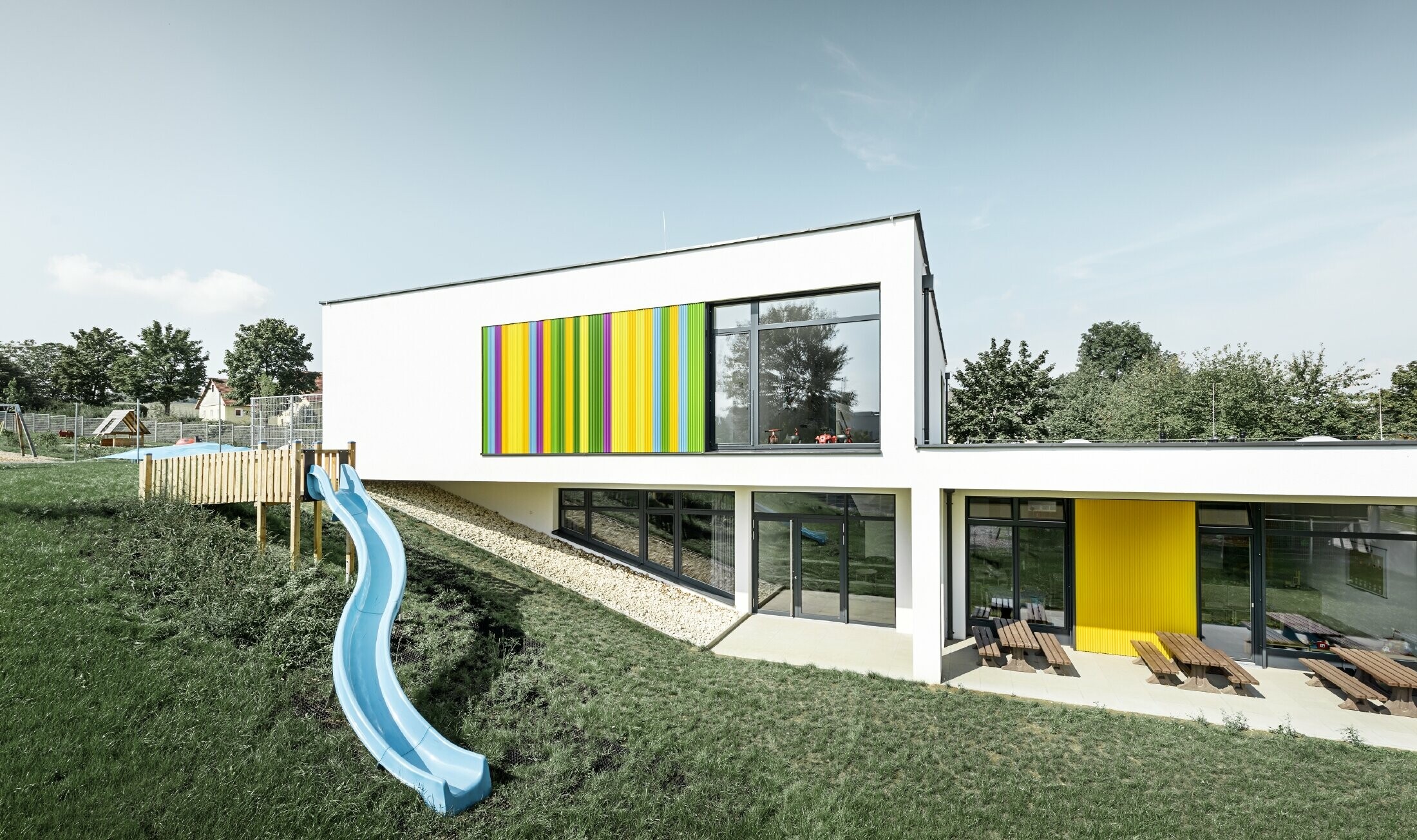 Zadní pohled na mateřskou školu v Hargelsbergu s fasádou z barevného Zackenprofil v barvách žlutá, zelená, fialová a modrá