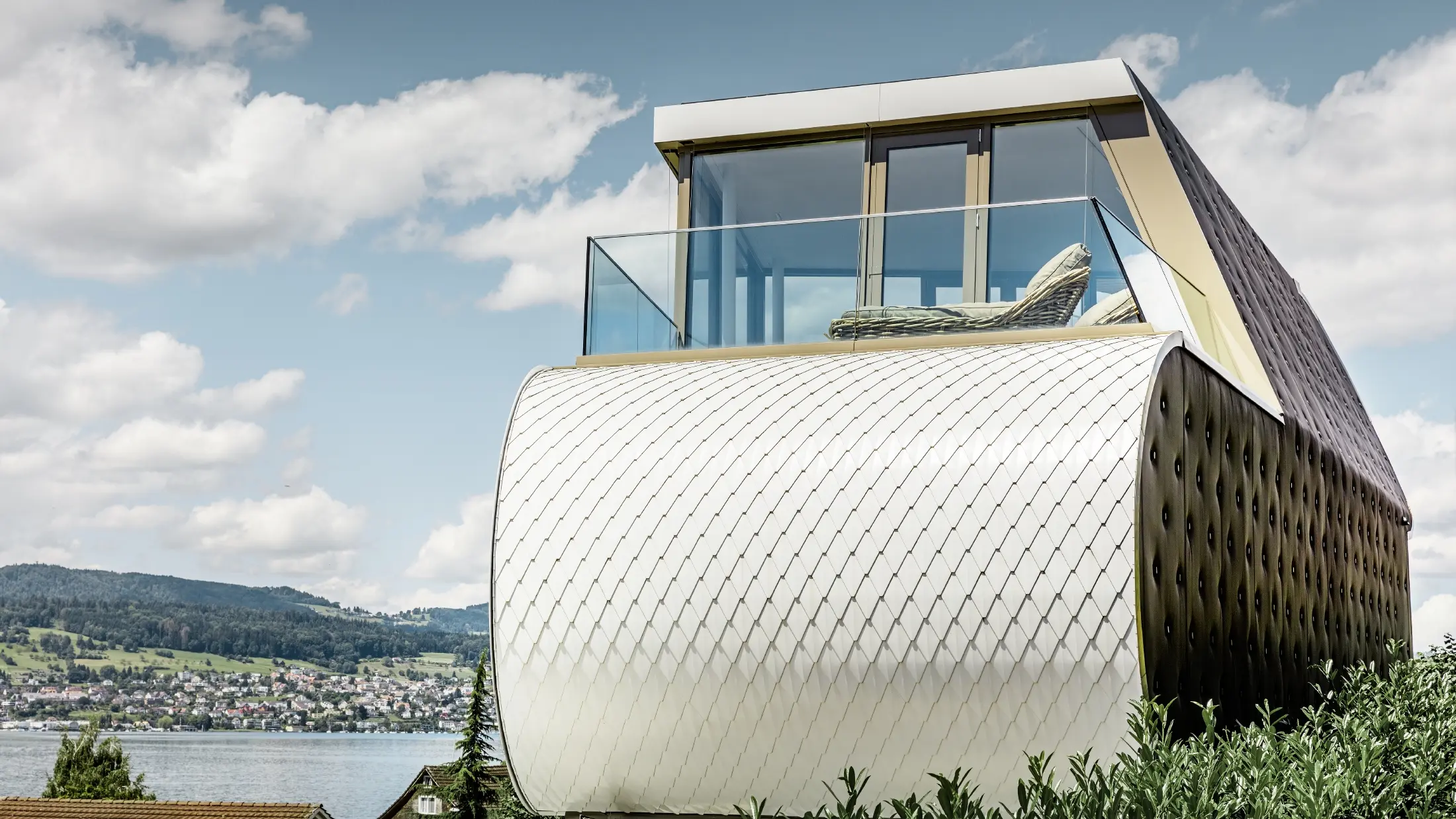 Boční pohled na oceněný Flexhouse, navržený architektem Camenzindem; je vidět jednu z oblých vnějších stěn, která je obložena šupinatou hliníkovou fasádou PREFA v čistě bílé barvě.