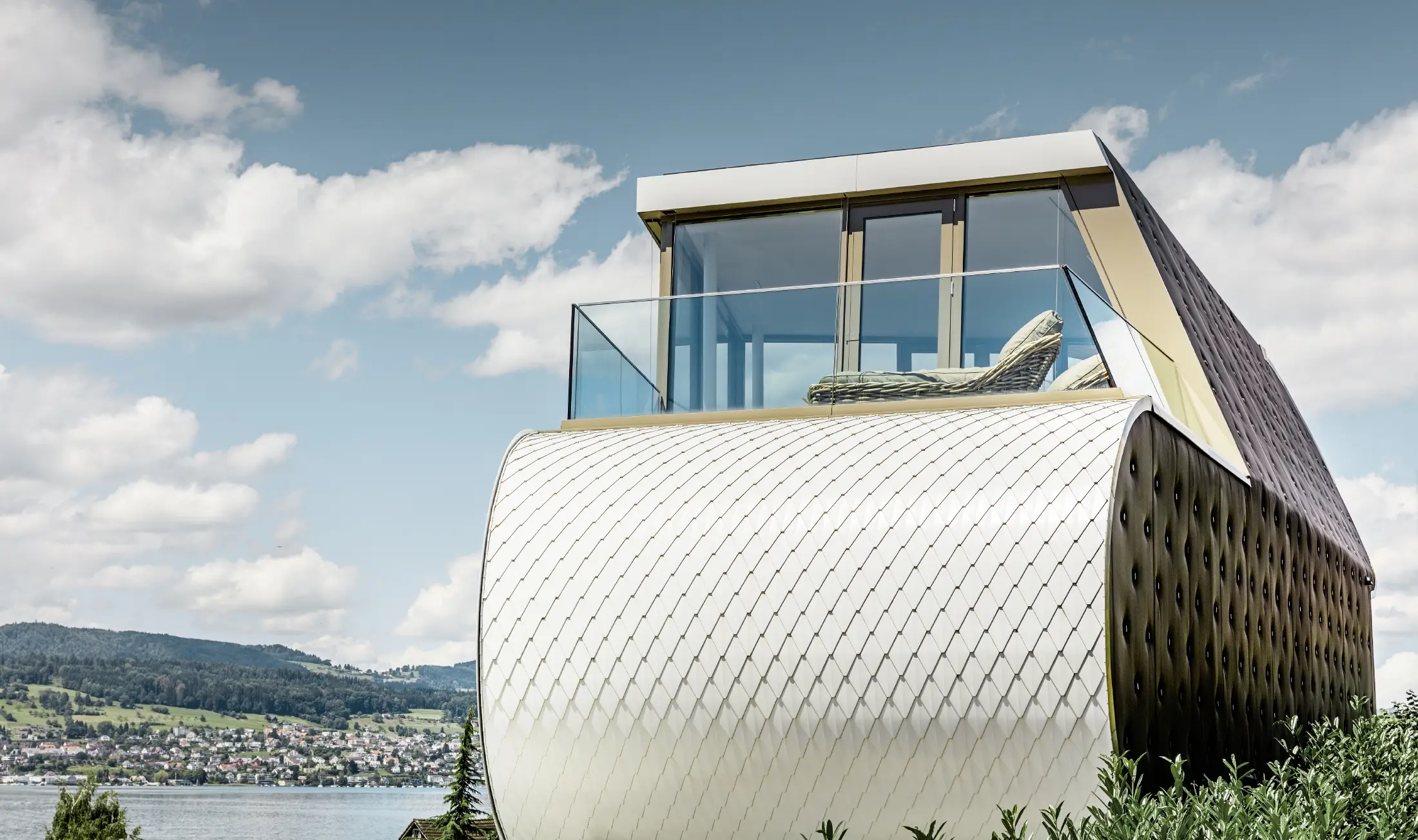 Boční pohled na oceněný Flexhouse, navržený architektem Camenzindem; je vidět jednu z oblých vnějších stěn, která je obložena šupinatou hliníkovou fasádou PREFA v čistě bílé barvě.