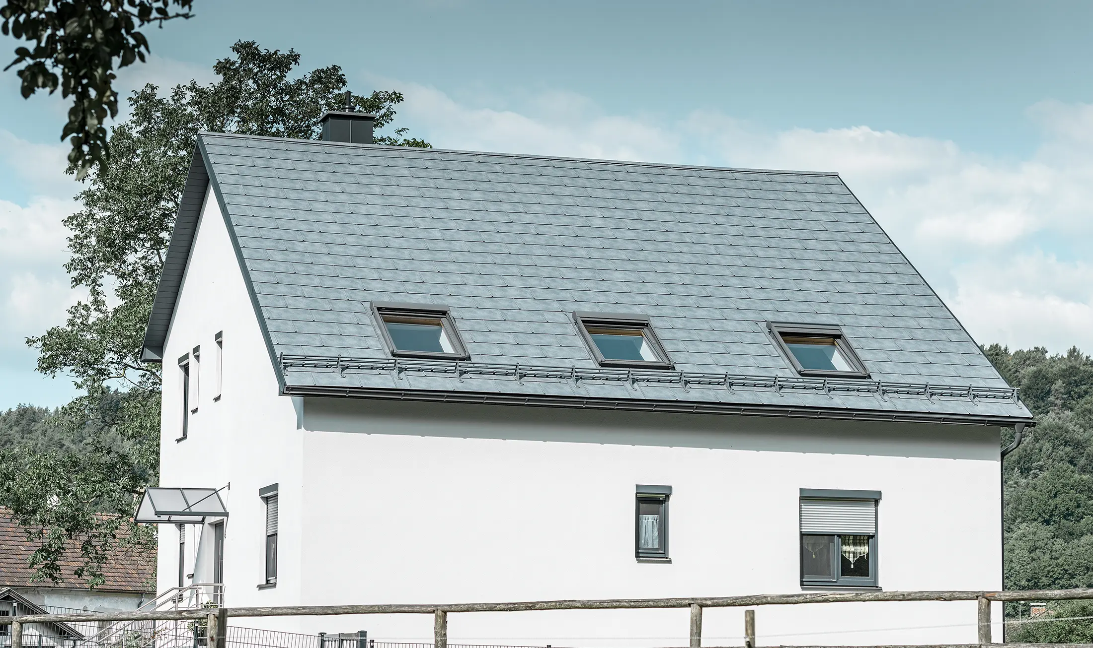 Sedlovou střechu klasického rodinného domu pokryl nový střešní panel PREFA R.16 v barvě P.10 břidlicové. Na ploše střechy se nachází také tři světlíky a protisněhové prvky. Fasáda je v bílé barvě.