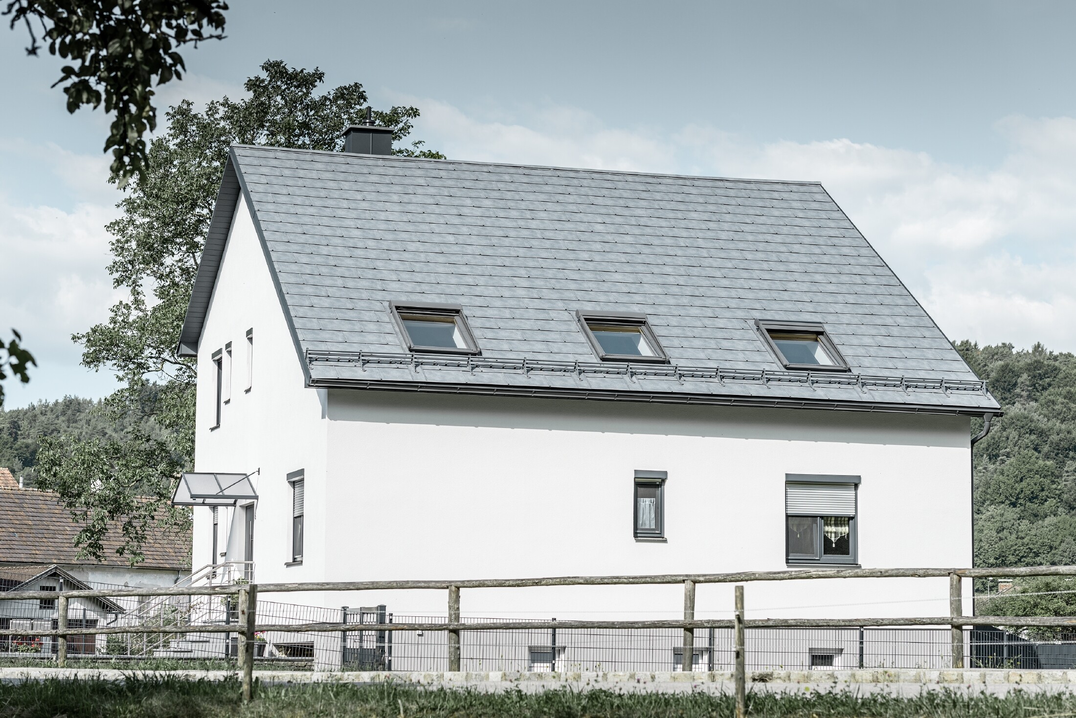 Sedlovou střechu klasického rodinného domu pokryl nový střešní panel PREFA R.16 v barvě P.10 břidlicové. Na ploše střechy se nachází také tři světlíky a protisněhové prvky. Fasáda je v bílé barvě.