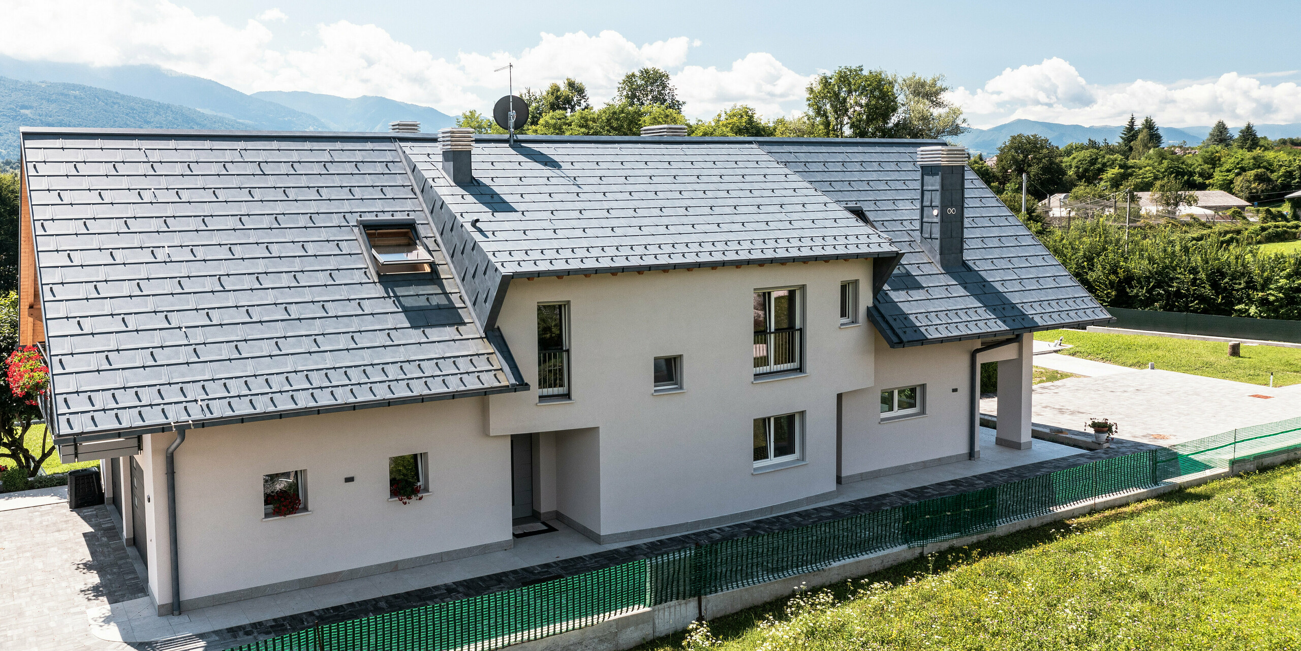Rodinný dům v Belluno, Itálie, s elegantní střechou PREFA ze střešních panelů R16 v barvě P.10 antracit. Systém odvodnění střechy sestávající z krabicového žlabu a odtokové trubky je barevně sladěn a dotváří estetický a funkční design střechy. Díky své tradiční konstrukci a modernímu střešnímu materiálu nabízí dům atraktivní kontrast na malebném horském pozadí.