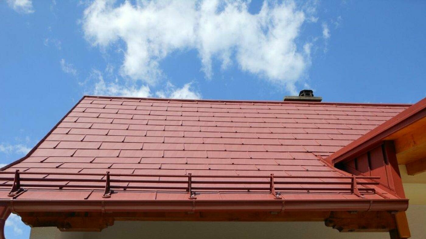 Detailní pohled na střechu s PREFA střešním panelem FX.12 v tmavě červené barvě se systémem sněhových zábran. 