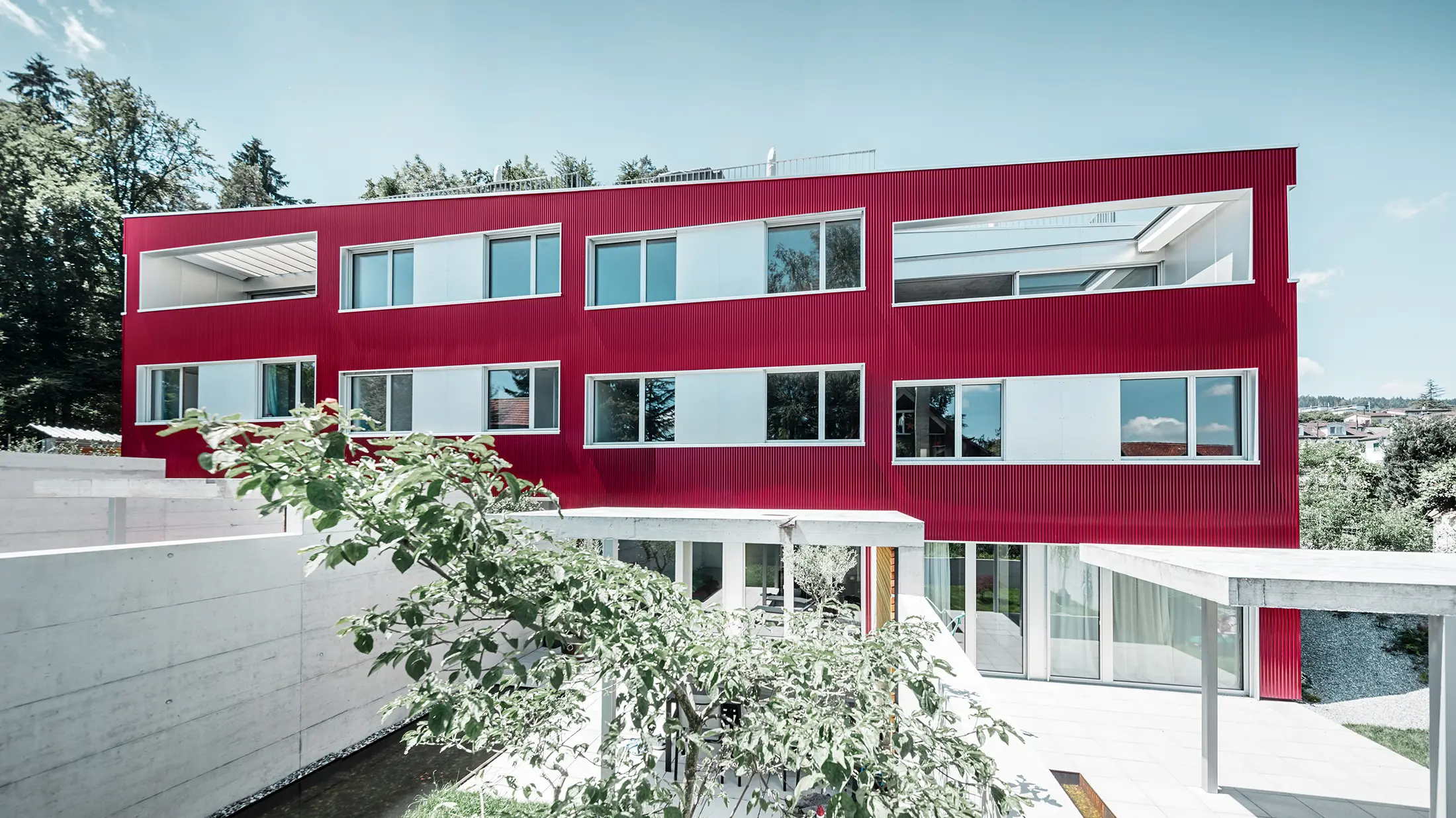 Bytový komplex s plochou střechou a balkony a vínově červenou fasádou s PREFA Profilwelle 