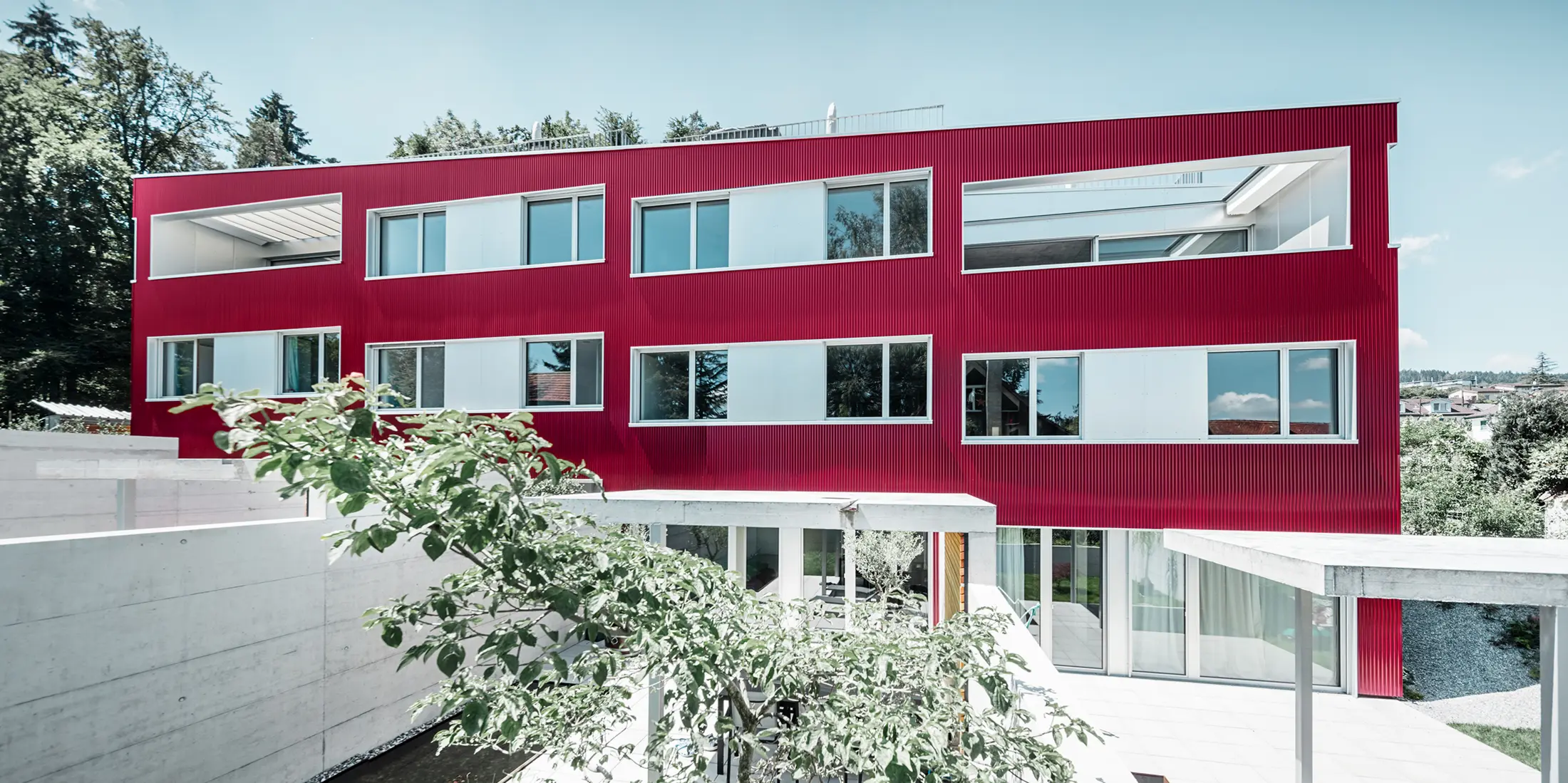 Bytový komplex s plochou střechou a balkony a vínově červenou fasádou s PREFA Profilwelle 