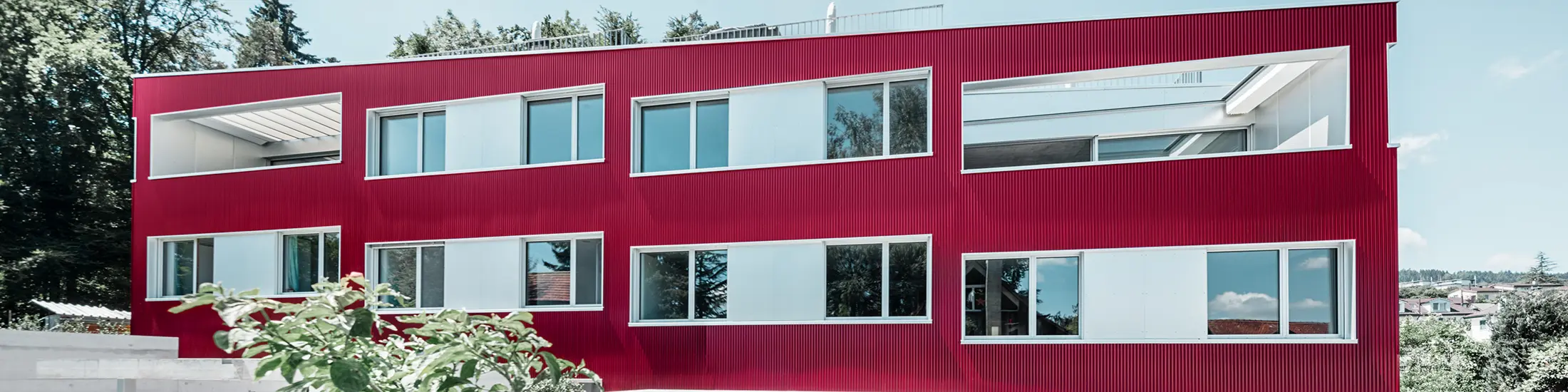 Bytový komplex s plochou střechou a balkony a vínově červenou fasádou s PREFA Profilwelle 