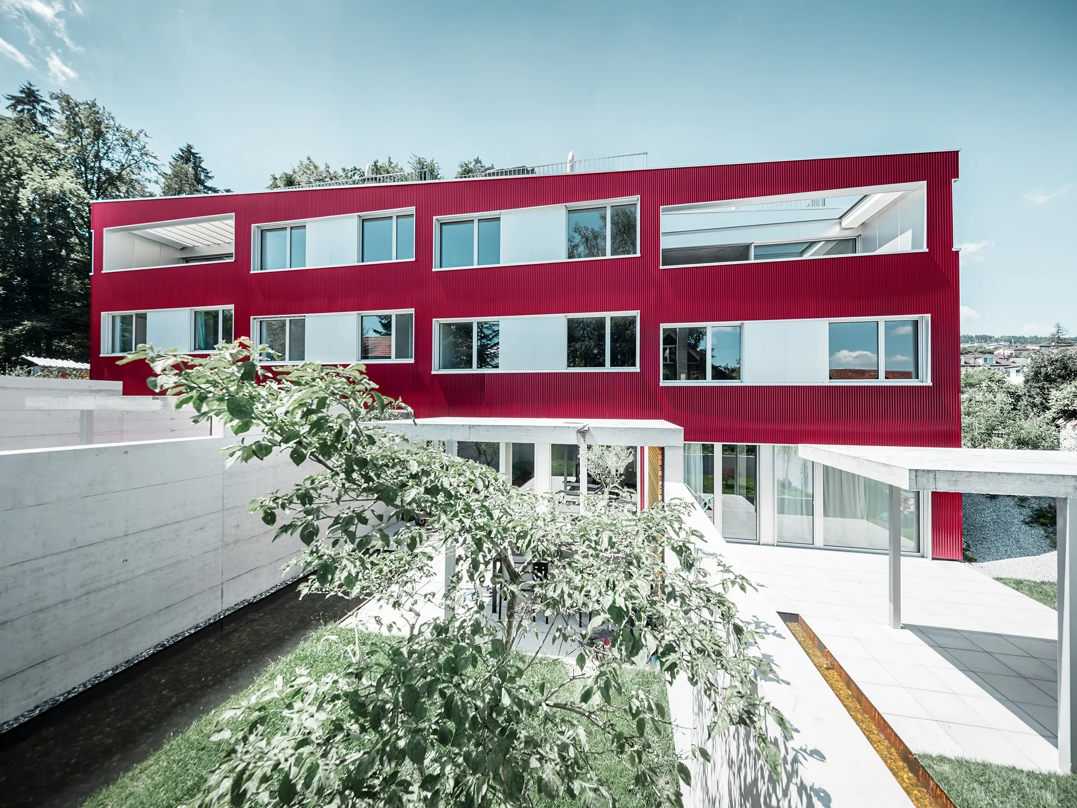 Bytový komplex s plochou střechou a balkony a vínově červenou fasádou s PREFA Profilwelle 