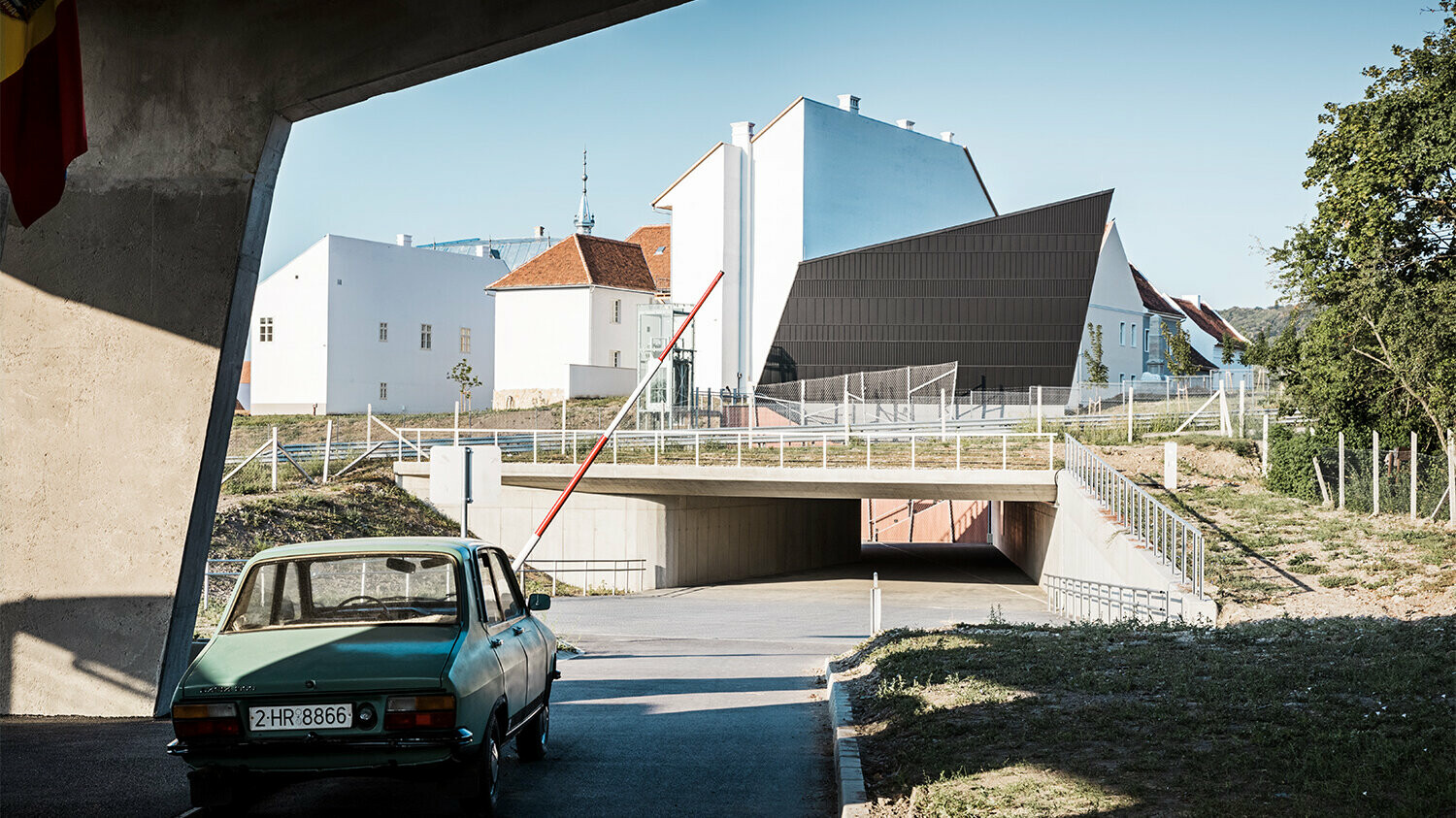 Boční pohled na část skanzenu včetně pavilonu kina, vlevo dole na snímku před ním projíždí příjezdovou cestou auto.