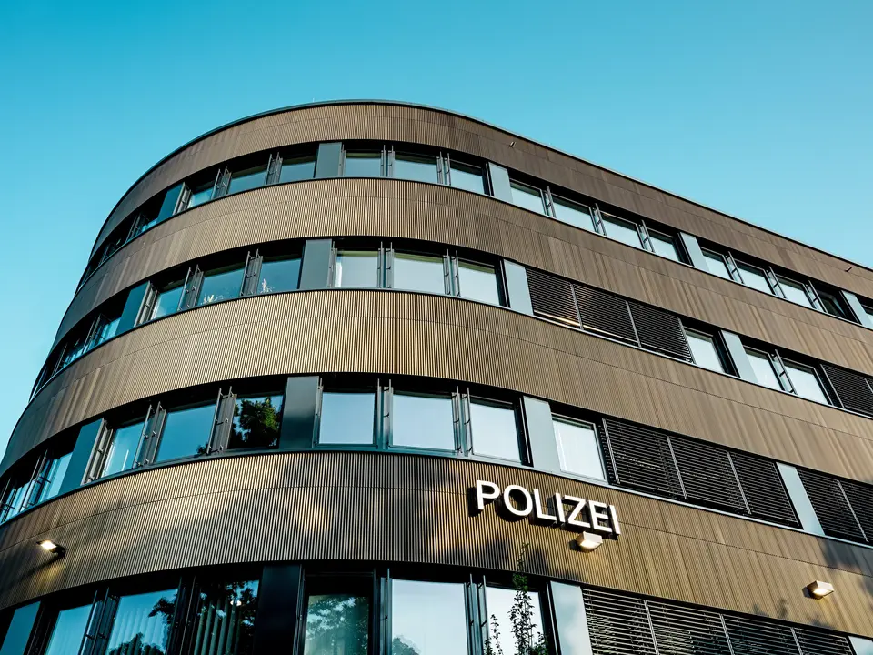 Dramatický pohled zdola na zakřivenou novostavbu policejní stanice 43 v Hamburku: Výrazná hliníková fasáda PREFA z eloxovaných extrudovaných profilů „Zacke“ ve střední bronzové barvě je architektonickým poutačem. Jemná, rytmická struktura vytváří dynamické světelné a stínové vzory a zdůrazňuje plynulé křivky budovy. Hliník PREFA nabízí vysokou odolnost proti povětrnostním vlivům, ochranu proti korozi a dlouhou životnost – udržitelné a nenáročné řešení pro precizní a moderní fasádní architekturu.
