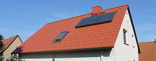 Rodinný dům se sedlovou střechou pokrytou PREFA falcovanými střešními taškami v cihlově červené barvě. Plocha střechy včetně solárního zařízení a střešního okna