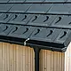 Detailní záběr PREFA střešních panelů R.16 se sněhovými háky, střešním žlabem a kruhovým svodem v provedení P.10 černá, včetně hromosvodu a svislé dřevěné fasády
