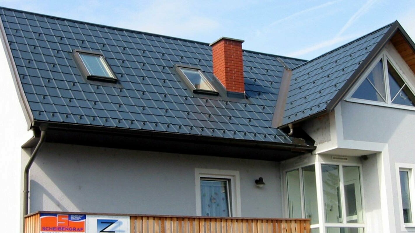 Rodinný dům s modrou fasádou se sedlovou střechou čerstvě sanovanou za použití produktů PREFA.