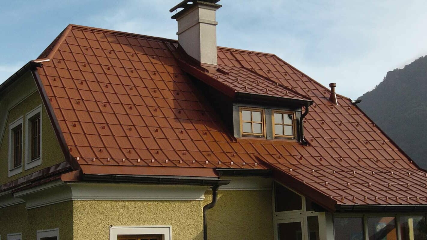 Rodinný dům s čerstvě sanovanou polovalbovou střechou a vikýřem za použití PREFA falcovaných střešních tašek v cihlově červené barvě.