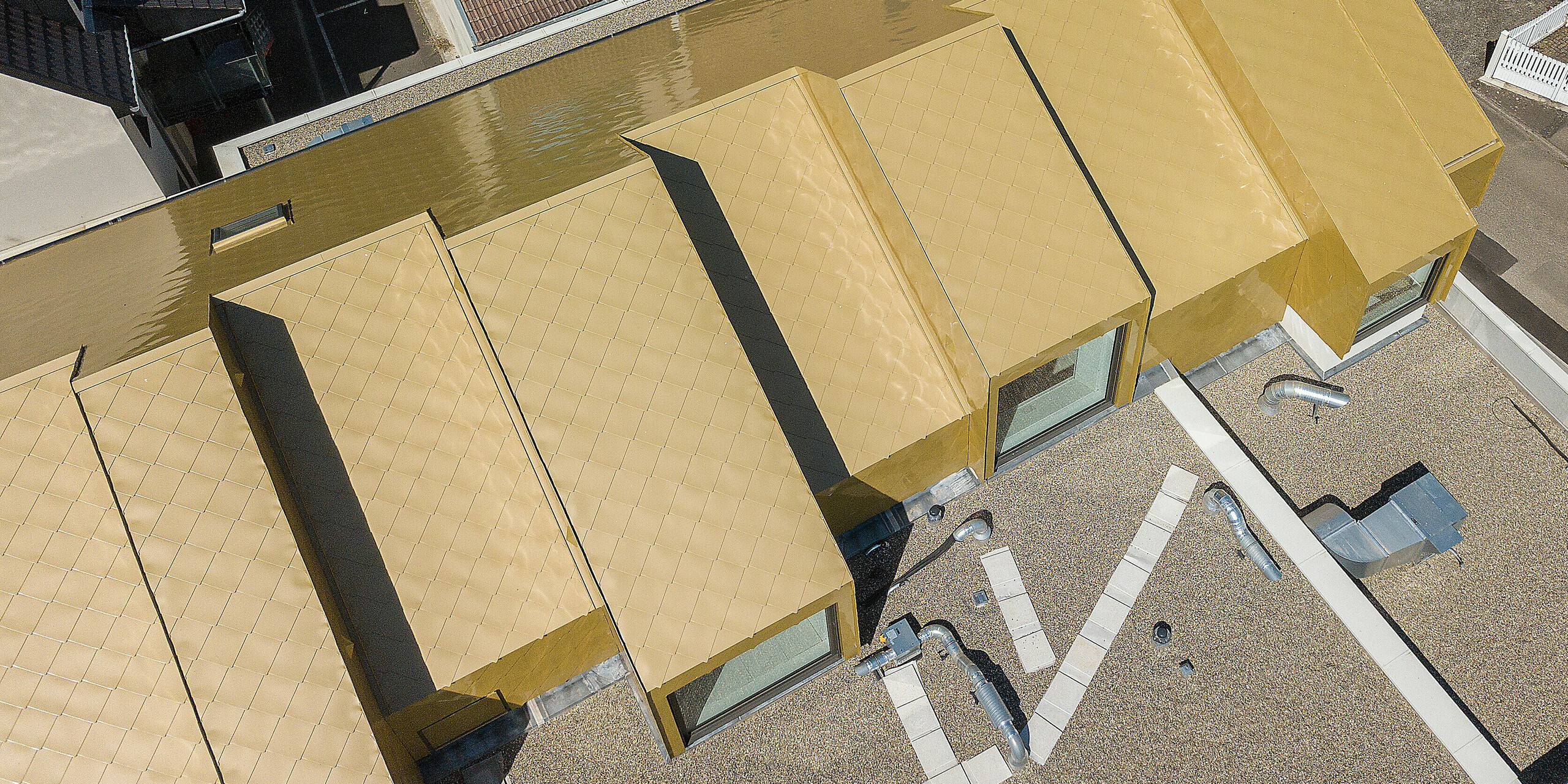 Pohled v výšky na střechu kulturního centra, které je opláštěno zlatými hliníkovými šablonami 44 x 44 od PREFA