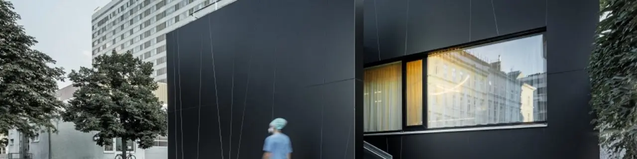 Frontalansicht der zentralen Notaufnahme der Klinik Landstraße in der Juchsgasse in Wien wurde mit PREFABOND Aluminium Verbundplatten in der Farbe schwarzgrau verkleidet. Im Bild ist eine Krankenschwester zu sehen.