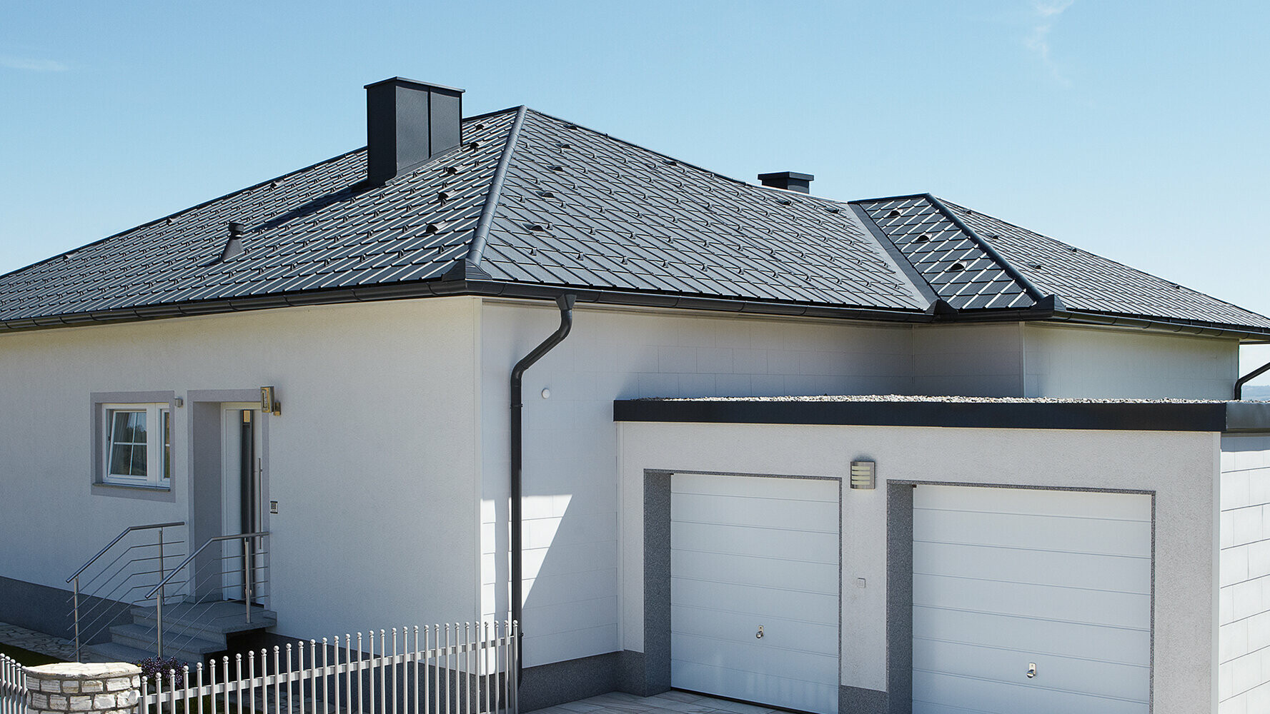 Sanace bungalovu s valbovou střechou pokrytou střešními panely PREFA v antracitové barvě. Vedle stojí dvojitá garáž.