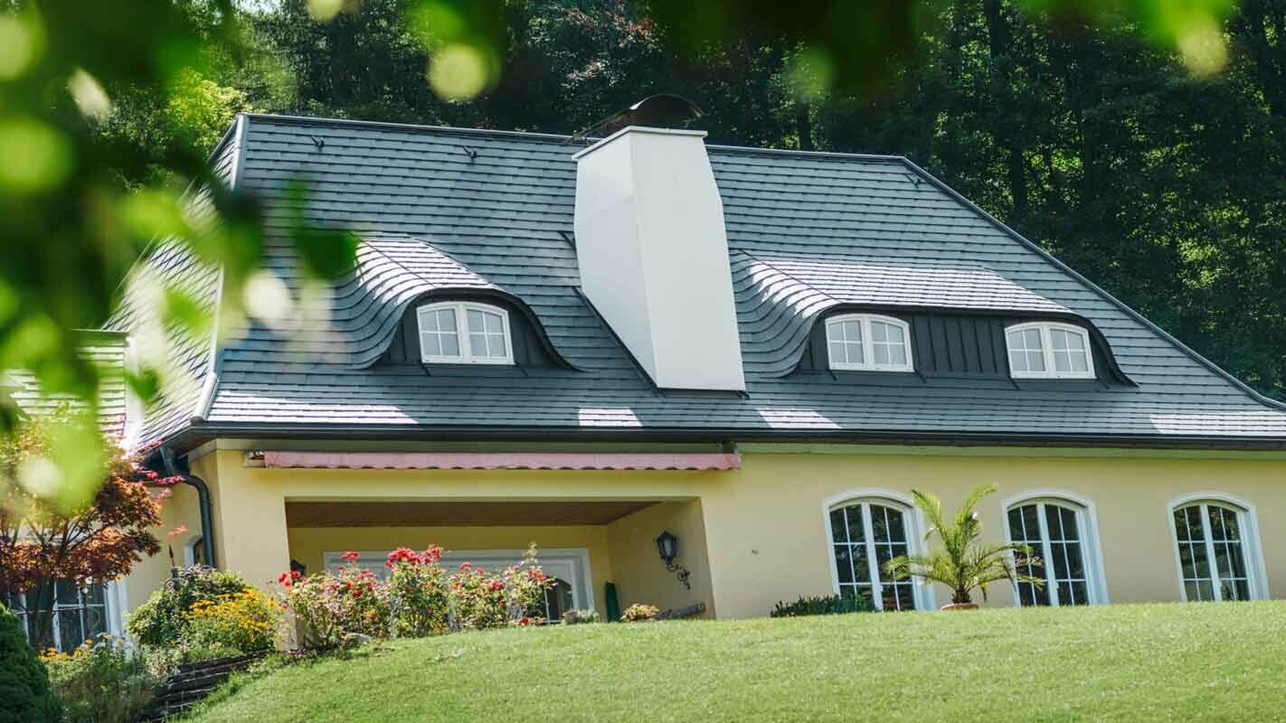 Střecha domu s velkým komínem a chmelovým vikýřem  po sanaci za použití PREFA falcovaných střešních šindelů 