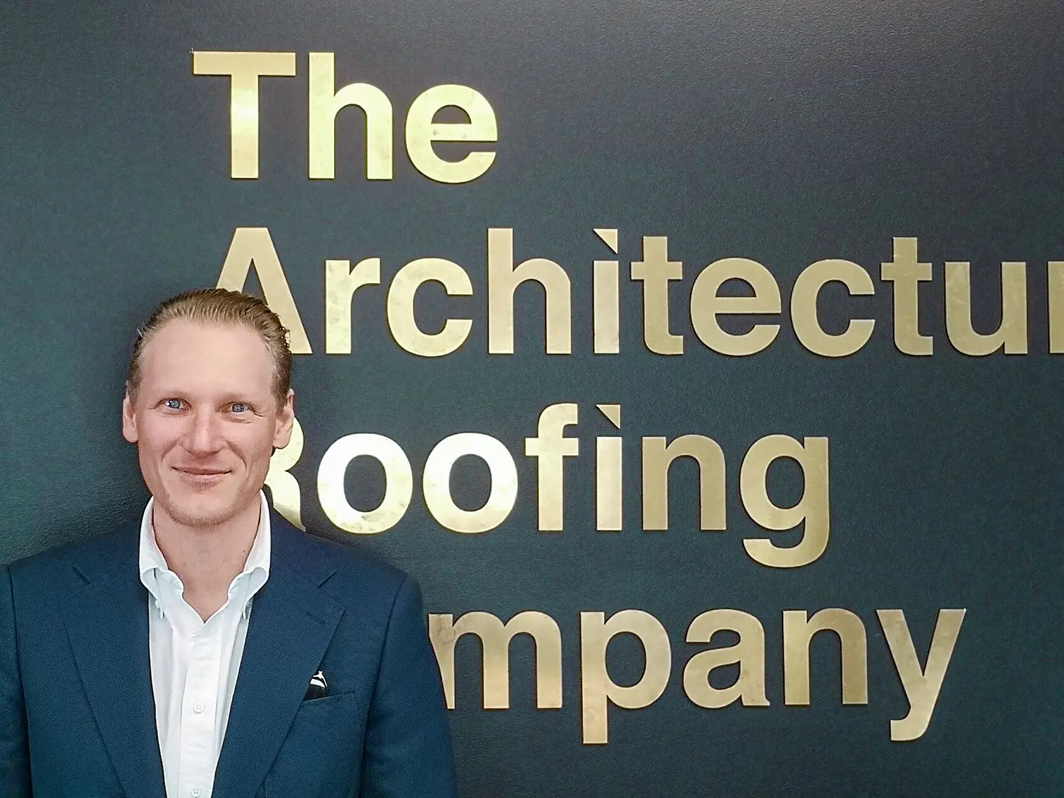 Portrét developera Johanna Vogla, v pozadí název firmy "The Architectural Roofing Company".