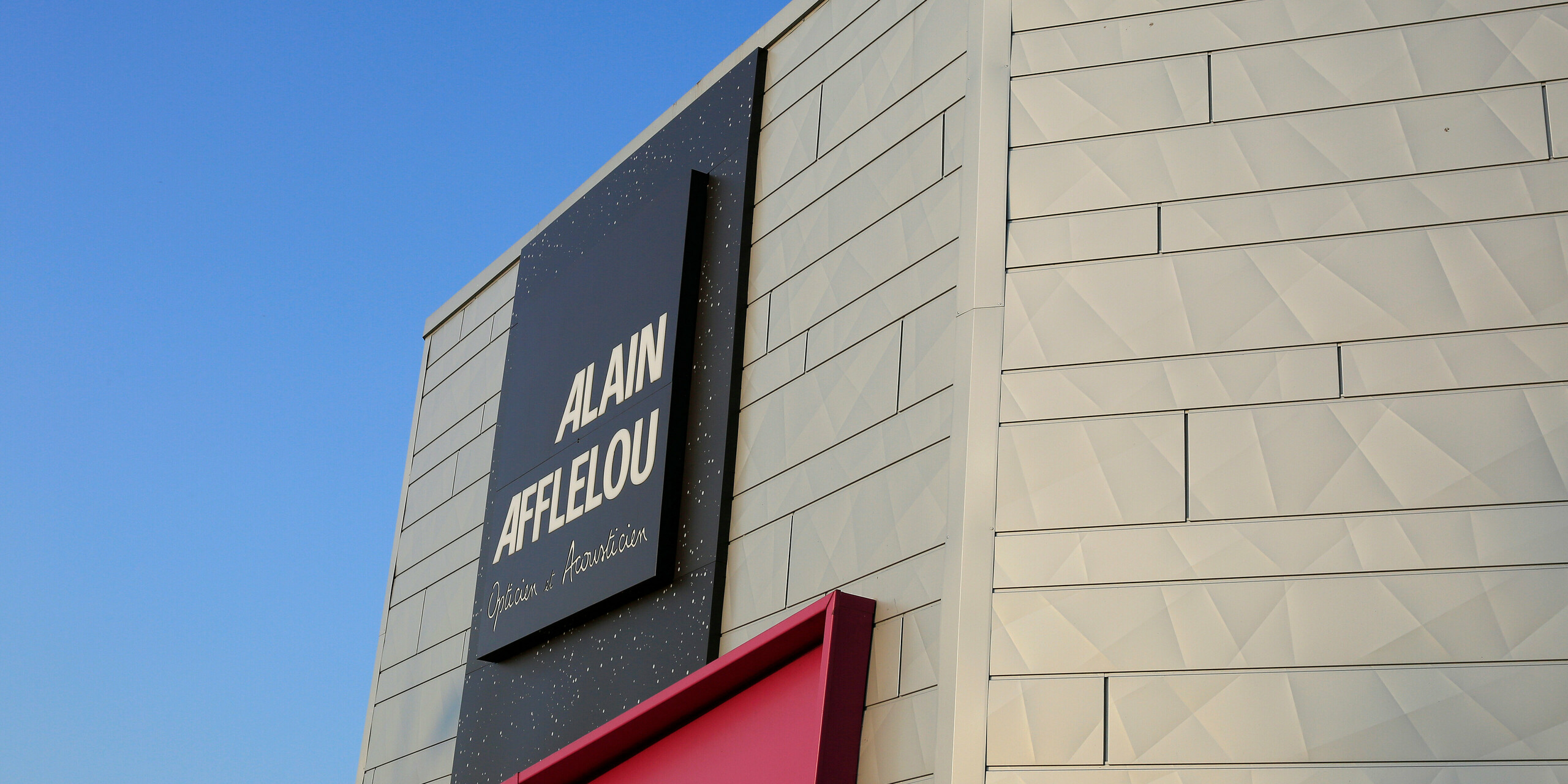 Boční detailní záběr na nápis společnosti AFFLELOU v obchodě v Auray se stříbrným hliníkovým pláštěm budovy