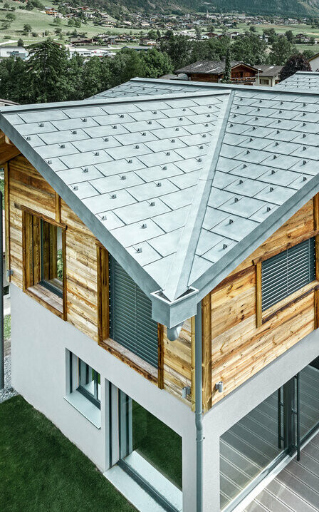 Švýcarská chata s hliníkovou střechou a dřevěnou fasádou. Dominantou střechy je střešní panel R.16.