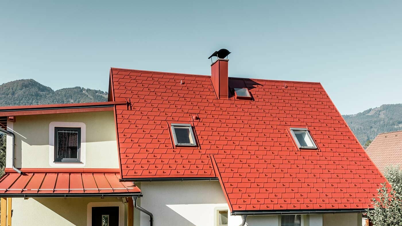Klasický rodinný dům s dvěma střešními okny a komínem, pokrytý novými PREFA falcovanými střešními šindeli DS.19 v barvě tmavě červená P.10.