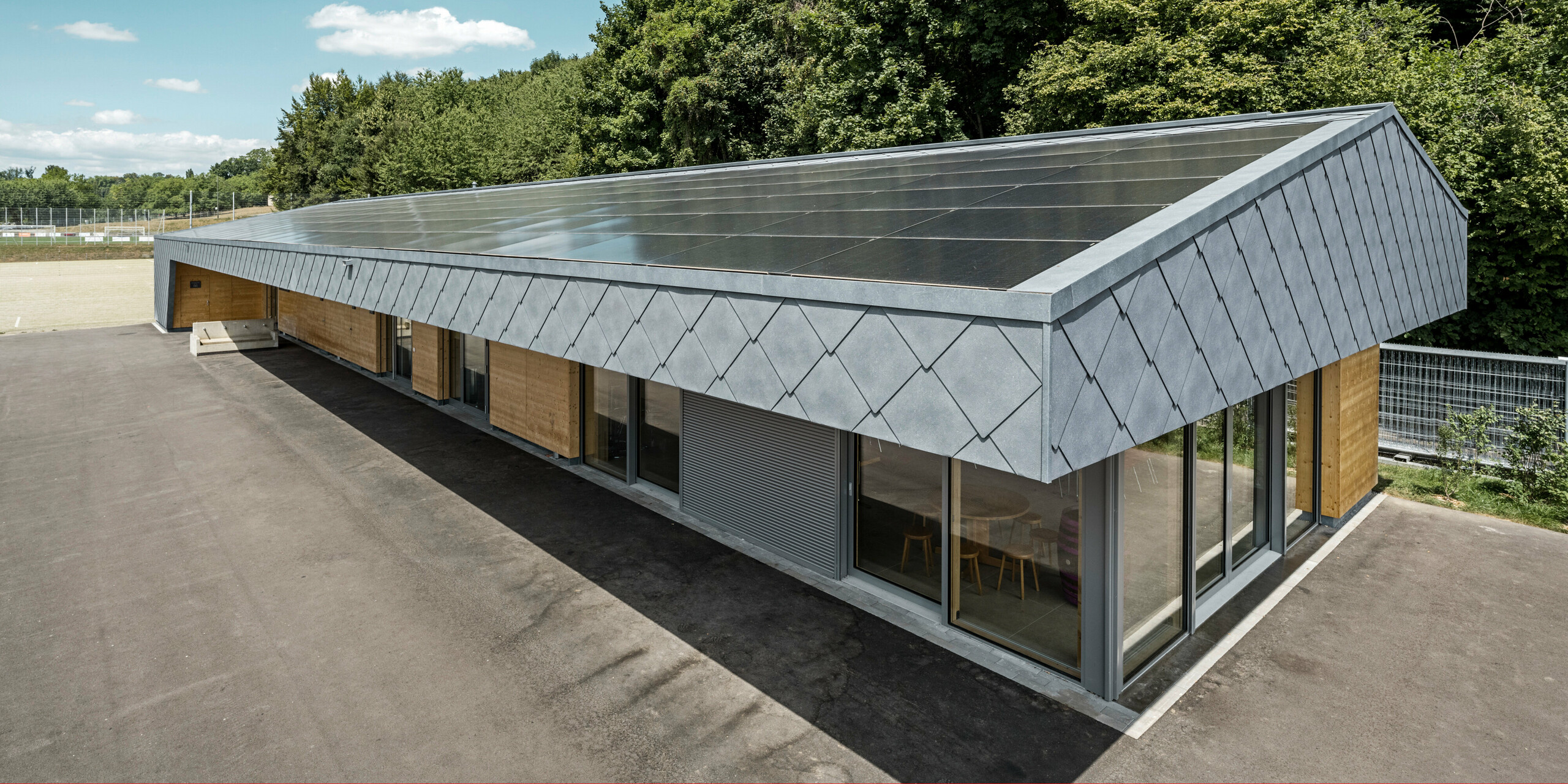 Das Gebäude einer Sportanlage in Prilly in der Schweiz wurde mit der PREFA Dach- und Wandraute 44x44 in P.10 Steingrau verkleidet. Auf dem Dach wurde großflächig eine Photovoltaikanlage montiert. 