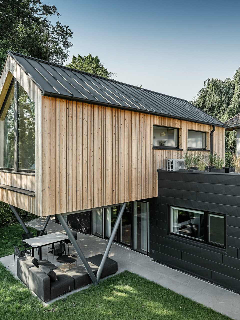 Boční pohled na objekt se sedlovou střechou z PREFALZ, dřevěnou fasádou a přístavby s fasádou Siding.X
