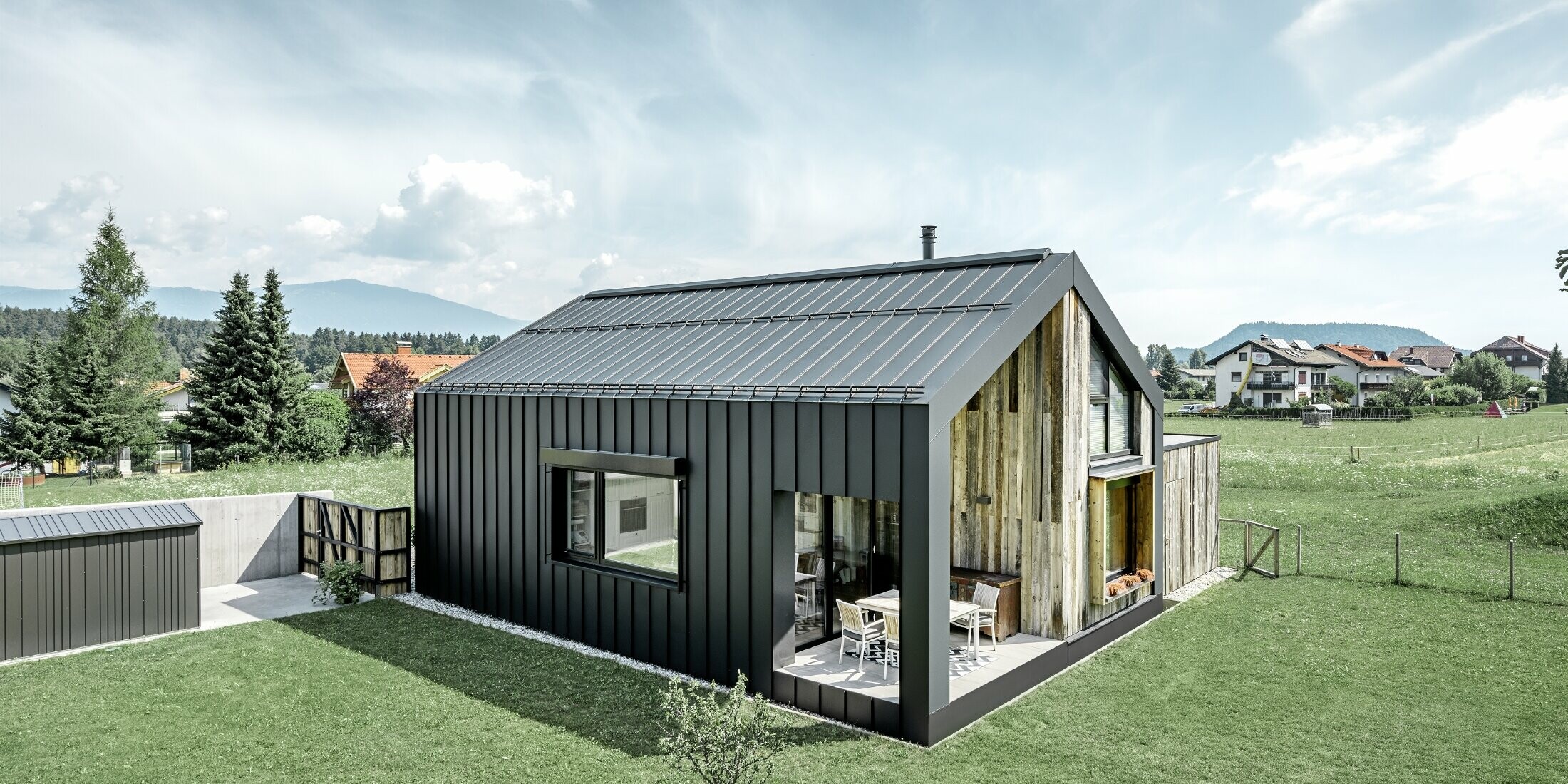 Rodinný dům se sedlovou střechou a fasádou pokrytou plechem PREFALZ v barvě P.10 antracit. Střecha plynule přechází do fasády, která je doplněna o dřevěné prvky.