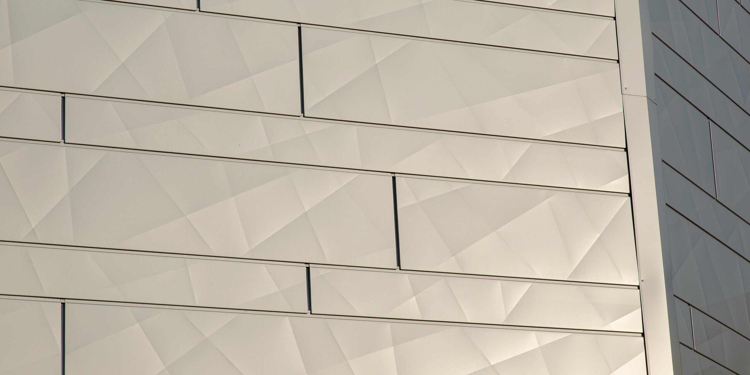 Detailní pohled na hranu budovy s třpytivými fasádními lamelami PREFA Siding.X ve stříbrné metalíze na budově v Auray ve Francii