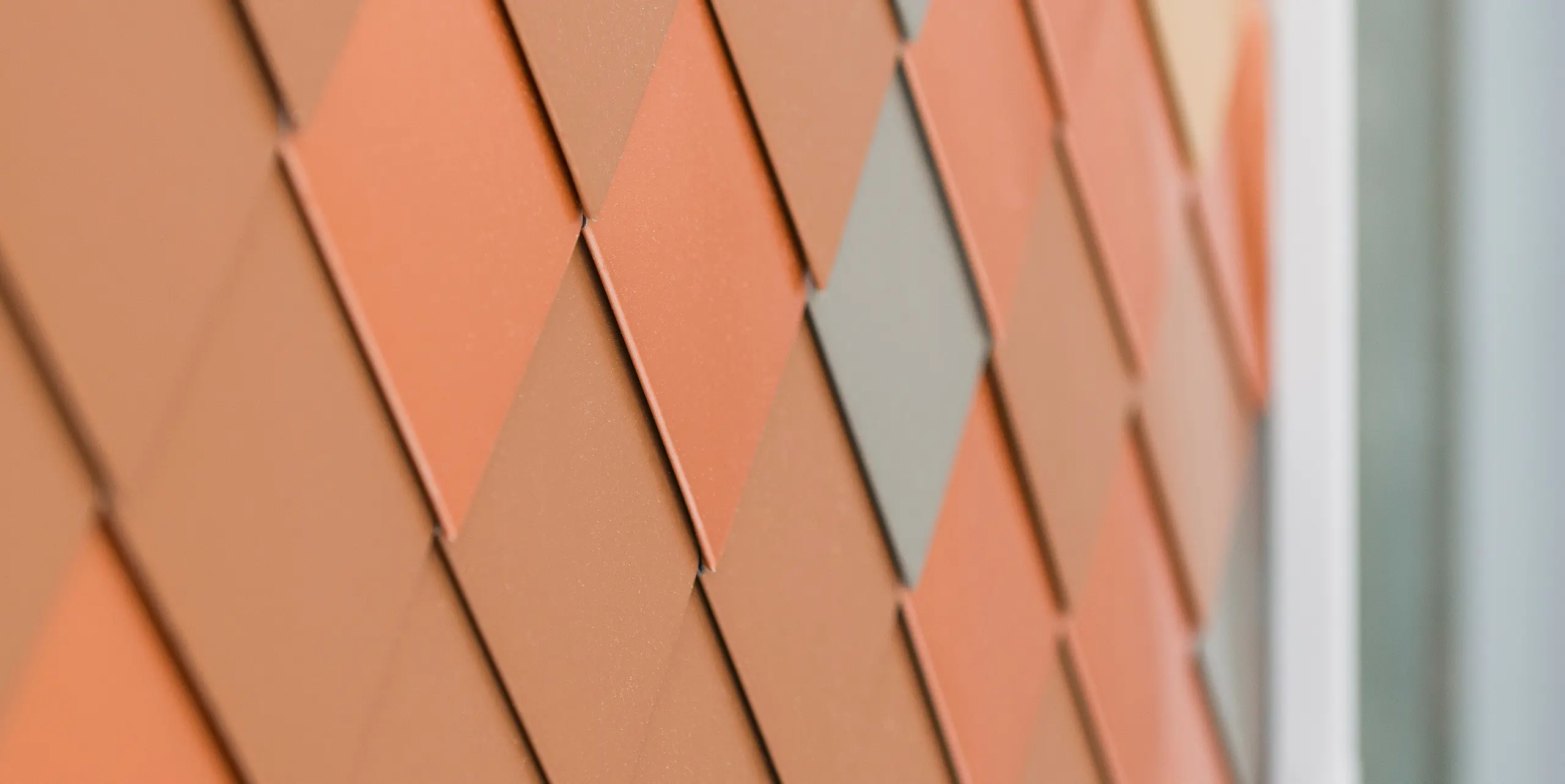 Detailní pohled na moderní hliníkovou fasádu PREFA s geometrickým vzorem v různých odstínech. Malé hliníkové fasádní šablony vytváří trojrozměrný vzhled, který zdůrazňuje strukturu a barevnou hloubku