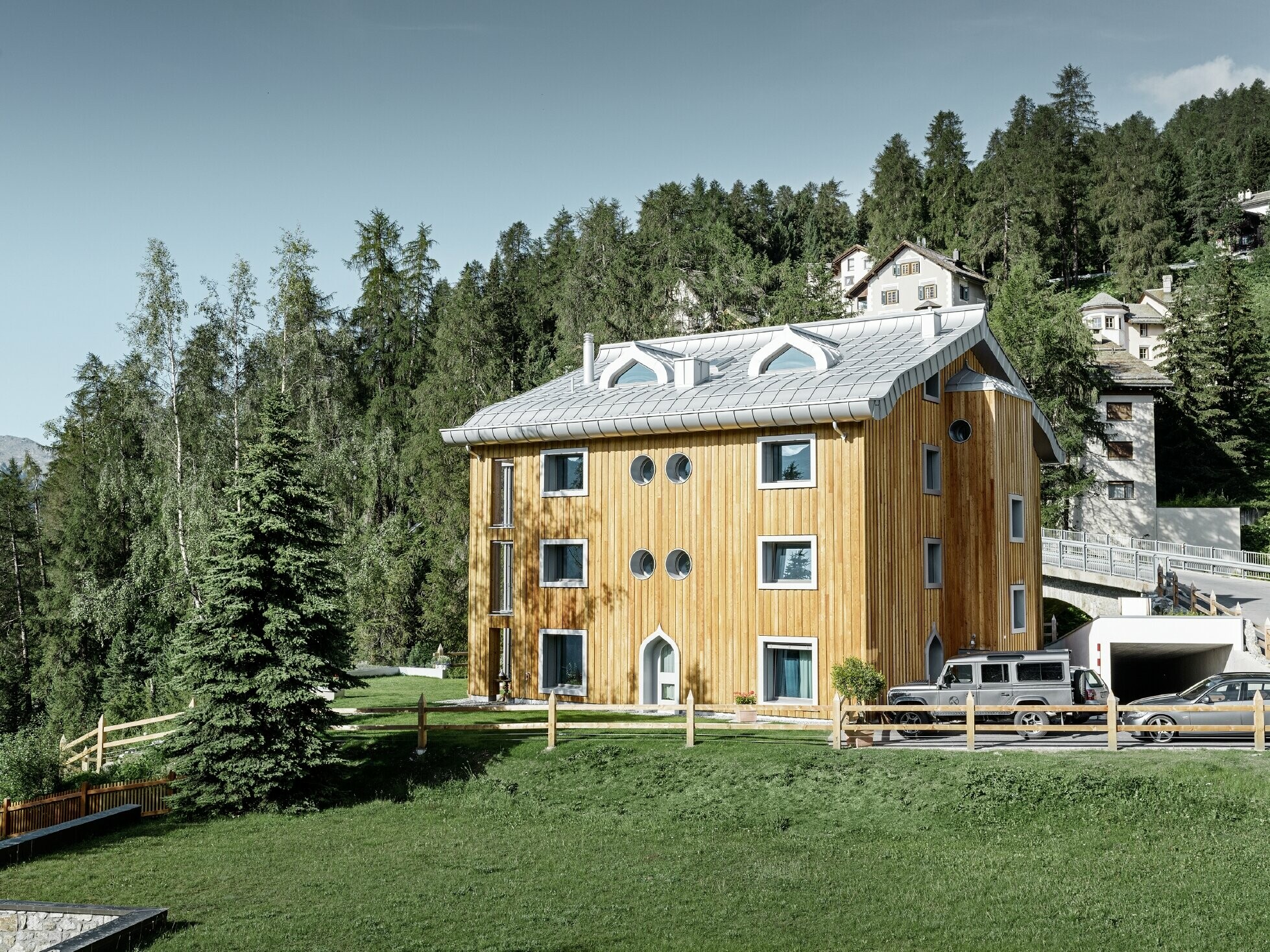 Wohnhausanlage in St. Moritz mit Holzfassade und Aluminiumdach mit geschwungener Traufe in silbermetallic