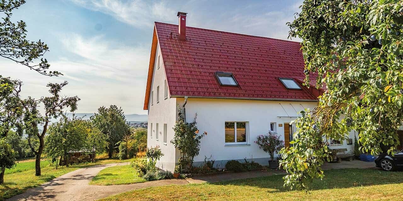 Romantická chalupa na venkově obklopená stromy a keři. Falcovaná taška PREFA je od klasické pálené téměř k nerozeznání.