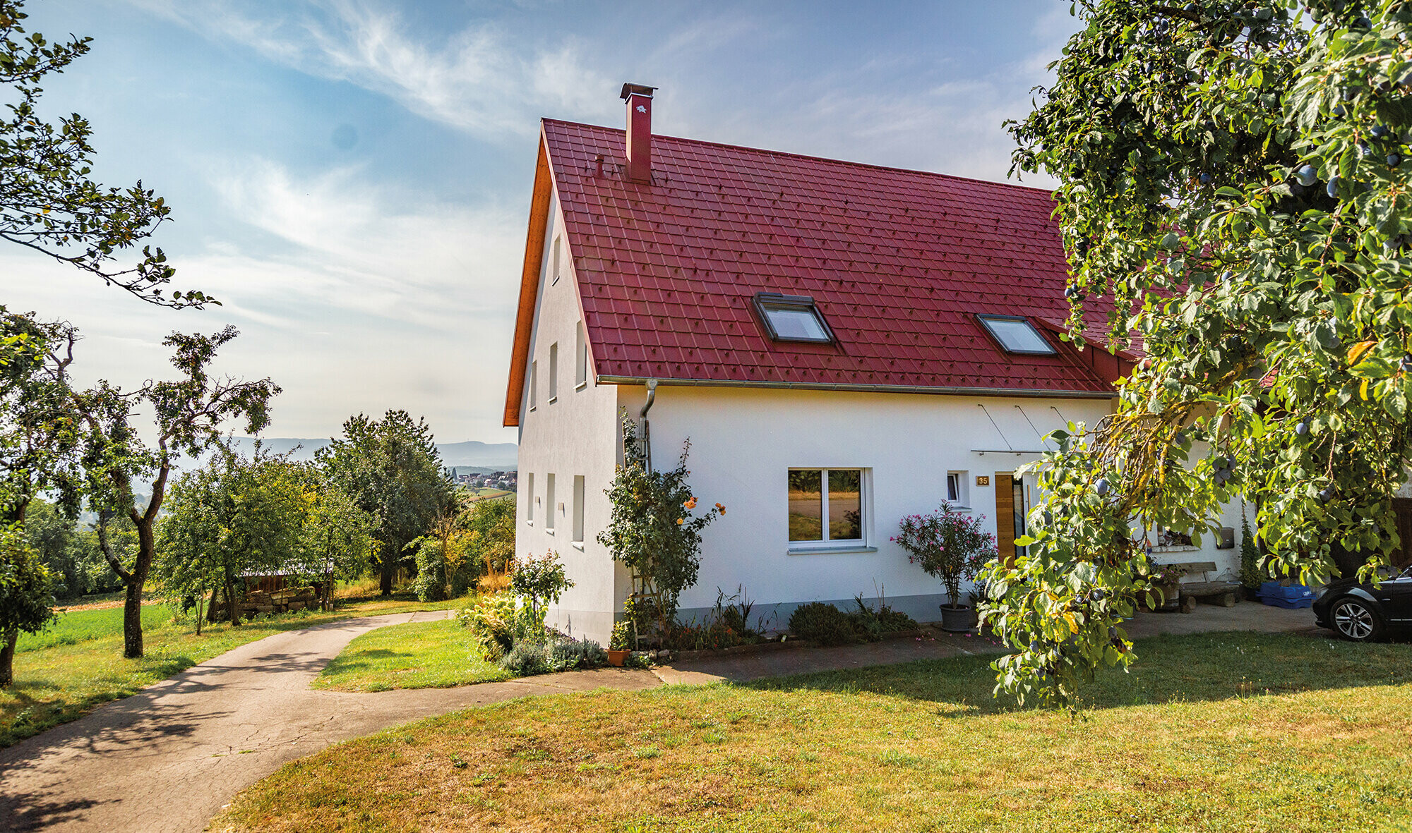Romantická chalupa na venkově obklopená stromy a keři. Falcovaná taška PREFA je od klasické pálené téměř k nerozeznání.
