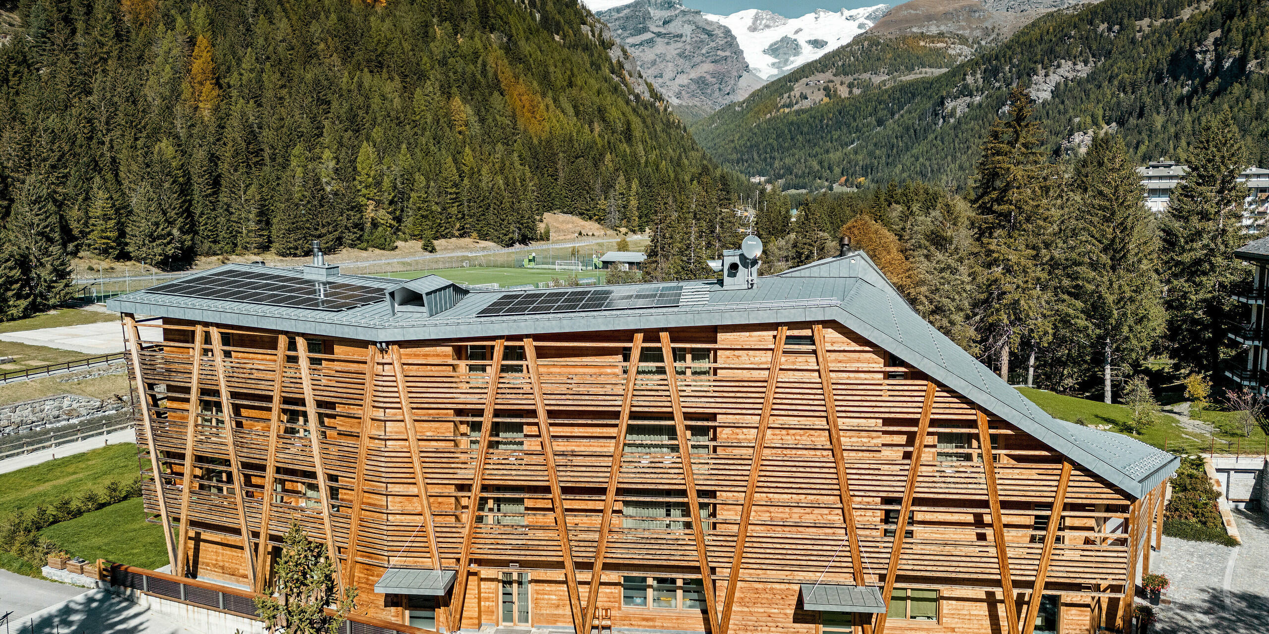 Das Hotel 'Au Charmant Petit Lac' in Champoluc präsentiert sich mit seiner charakteristischen Holzfassade und einem PREFALZ Aluminiumdach in P.10 Steingrau, das durch die Integration von Solarmodulen eine umweltbewusste Energiegewinnung ermöglicht. Die Konstruktion fügt sich harmonisch in die alpine Umgebung ein und spiegelt die Verpflichtung des Hotels zu Nachhaltigkeit und natürlicher Ästhetik wider. Die klaren Linien des Daches und die natürliche Textur der Holzelemente erzeugen eine visuelle Synergie, die Modernität und Tradition vereint.