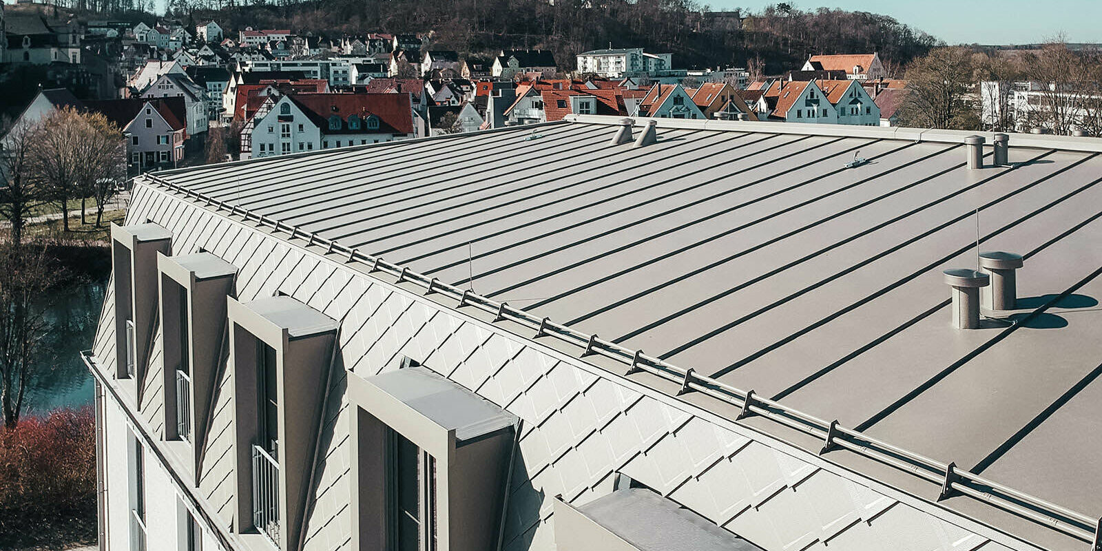 Pohled na plochu střechy s falcovanými šablonami 29 × 29 na stěnách valbové střechy a hliníkové šáry plechu PREFALZ střeše s mírným sklonem.