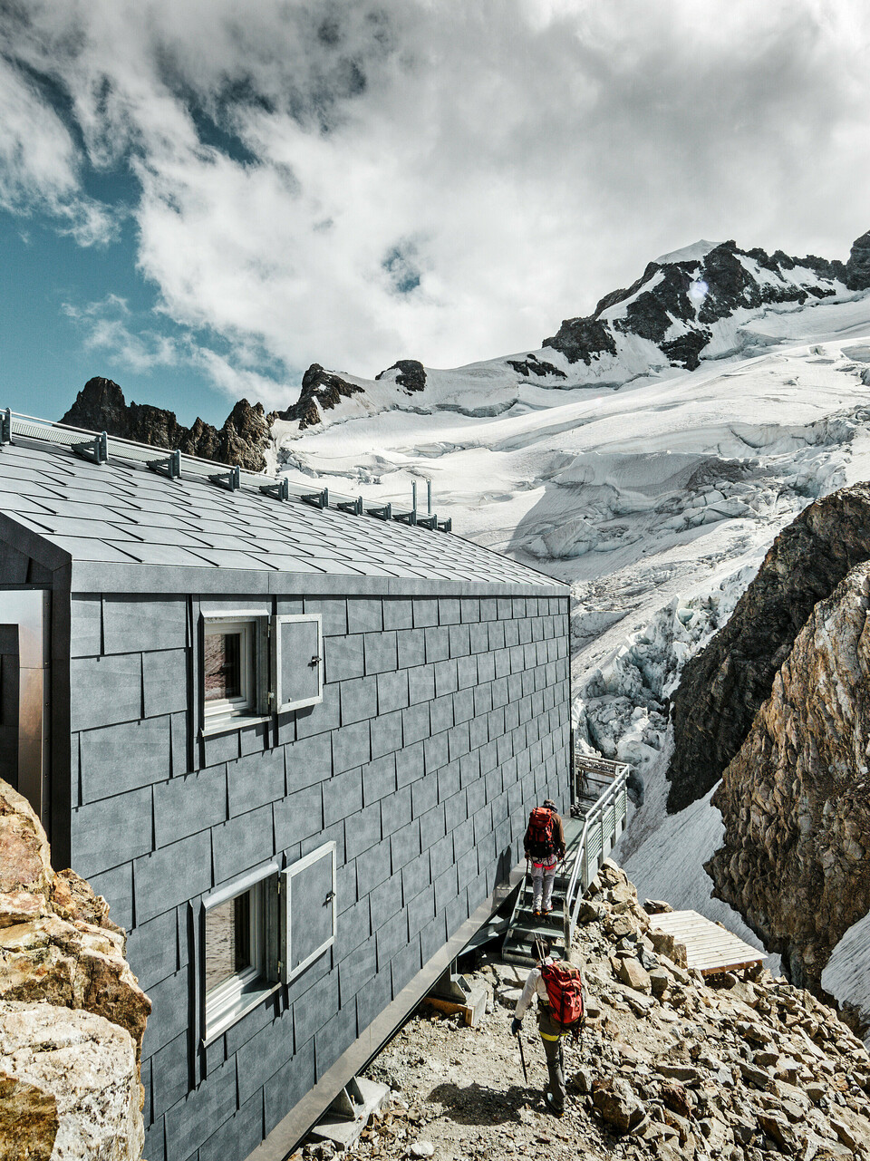 Seitliche Ansicht der Refuge de l'Aigle Berghütte mit steingrauen FX.12 Dach- und Fassadenpaneelen von PREFA, eingebettet in eine beeindruckende Gletscherlandschaft.