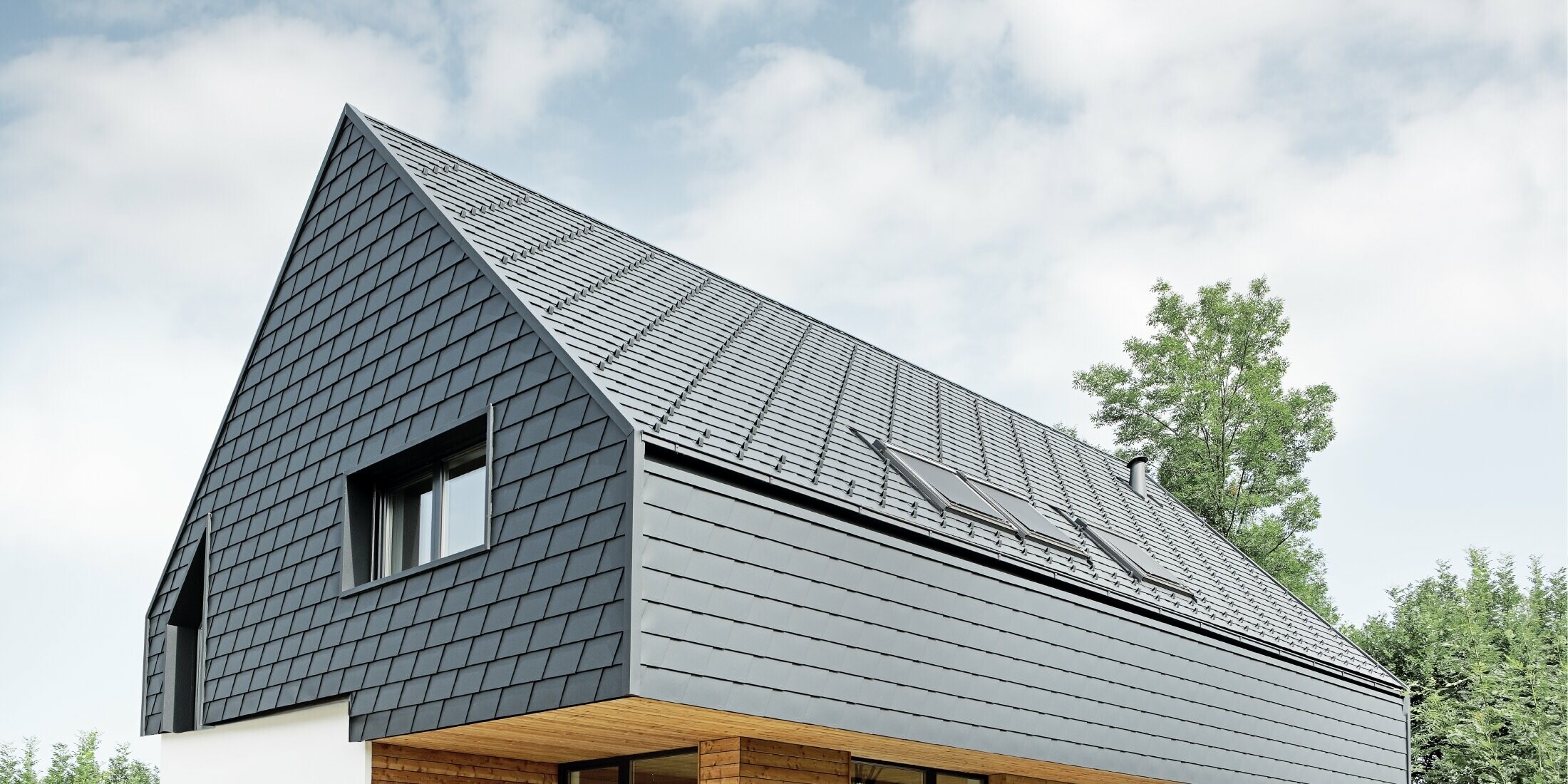 Rodinný domek se sedlovou střechou, pokrytý PREFA šindelem v barvě P.10 antracitové; šindele jsou použity také na fasádě v horním podlaží a na štítu