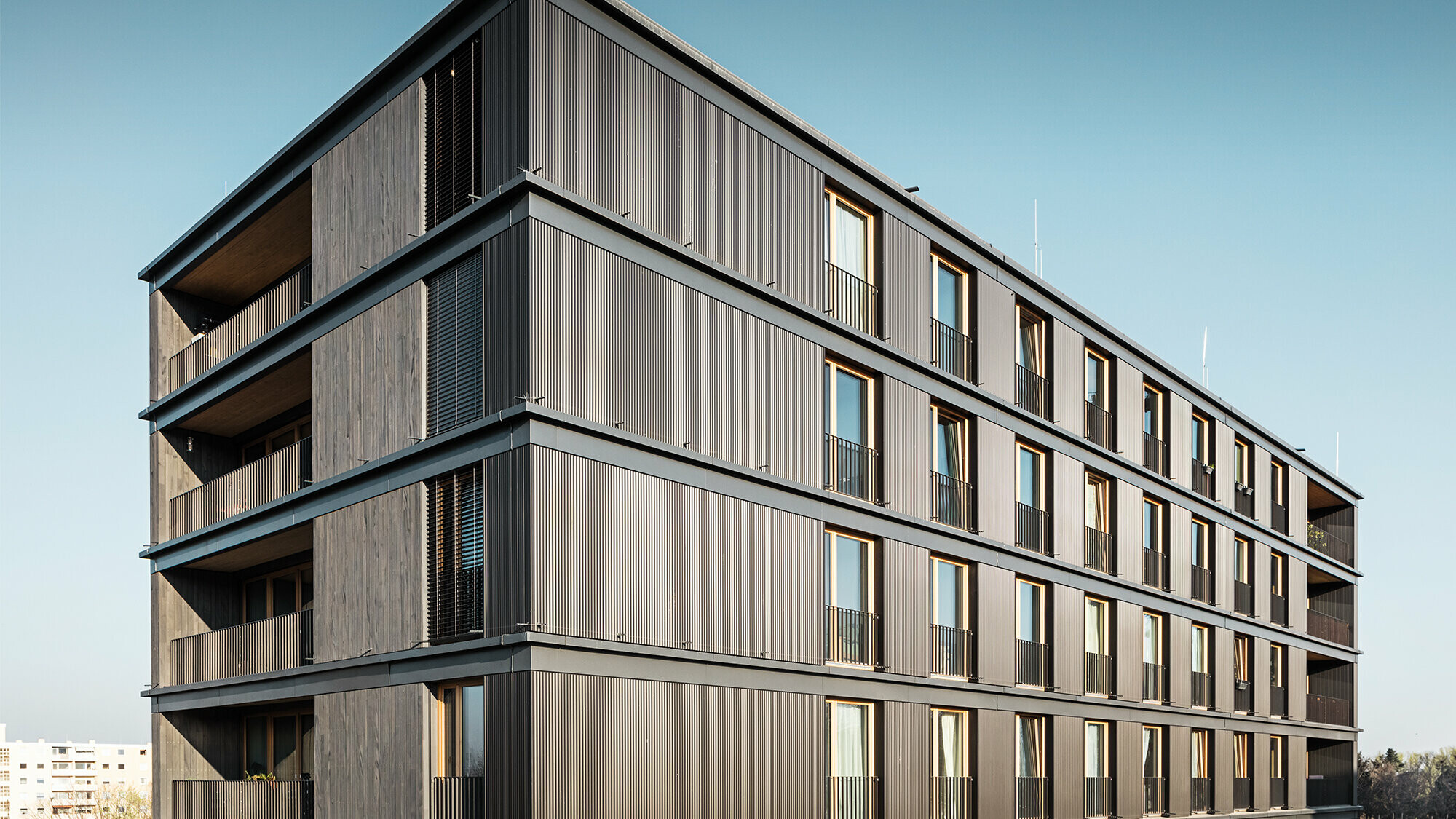 Komerční a bytový dům z bočního pohledu. Východní stěna fasády je opláštěna lisovaným profilem s vlnou v černošedé barvě od PREFA