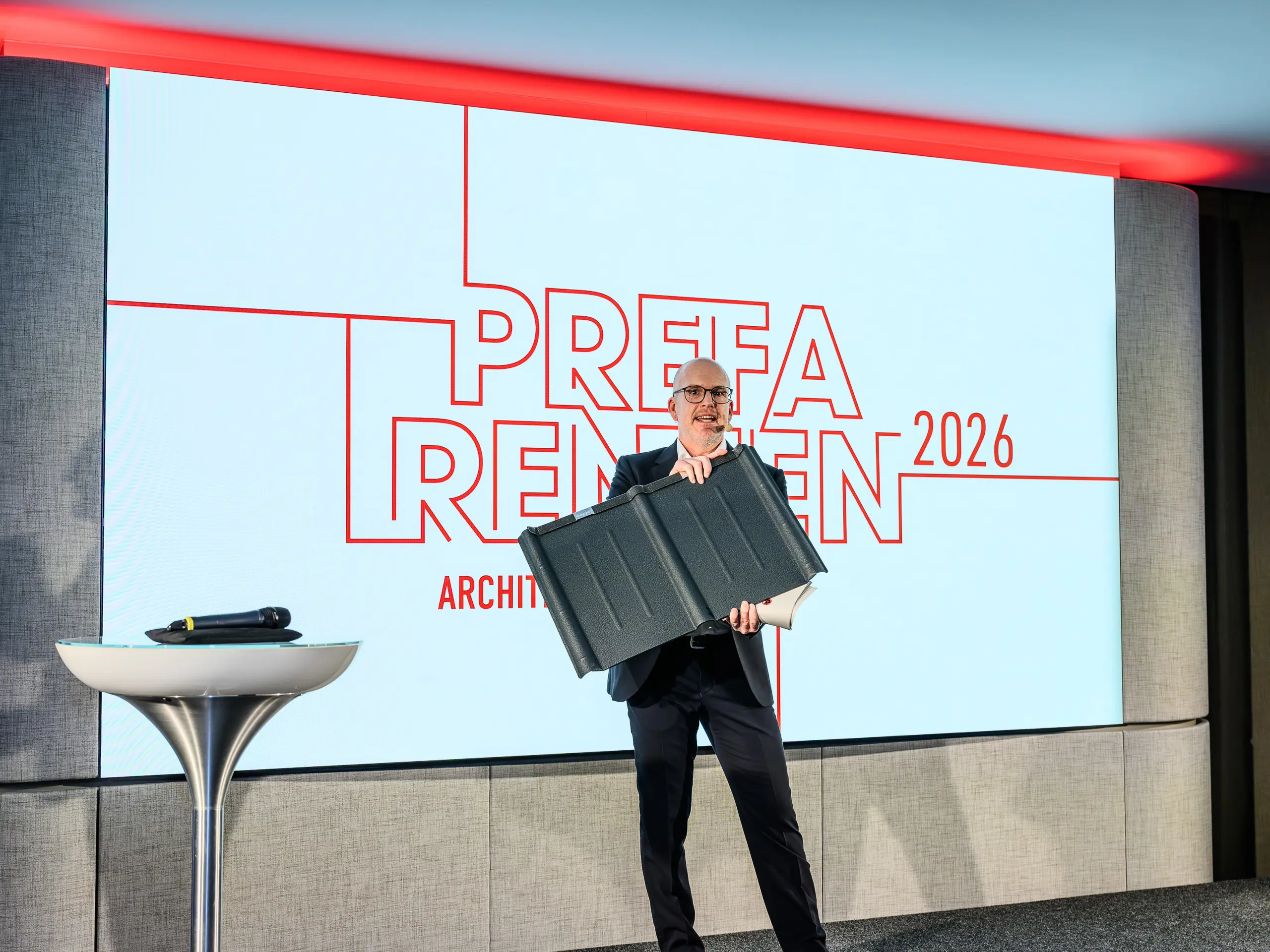 Vrcholem prezentace PREFARENZEN 2026 je Jürgen Jungmair, mezinárodní marketingový ředitel PREFA, který hrdě představuje ikonickou falcovanou tašku PREFA. V centru pozornosti je tento odolný hliníkový produkt, který se úspěšně vyrábí již přibližně 80 let. Moderní pódium s charakteristickým logem PREFARENZEN podtrhuje význam produktu pro architekturu budoucnosti. Lehký, odolný vůči bouřím a nerezavějící – střešní panel PREFA spojuje technologii a estetiku na nejvyšší úrovni.