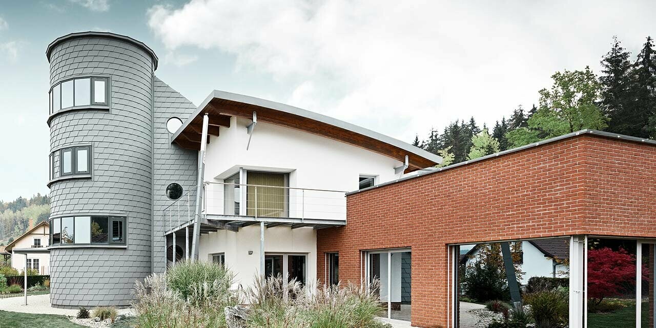 Einfamilienhaus mit Turmzubau, der runde Turm ist mit der PREFA Wandschindel in Patina Grau verkleidet 