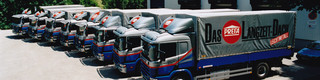 V jedné řadě se prezentuje osm někdejších modrých a stříbrných nákladních vozů firmy s logem PREFA.  