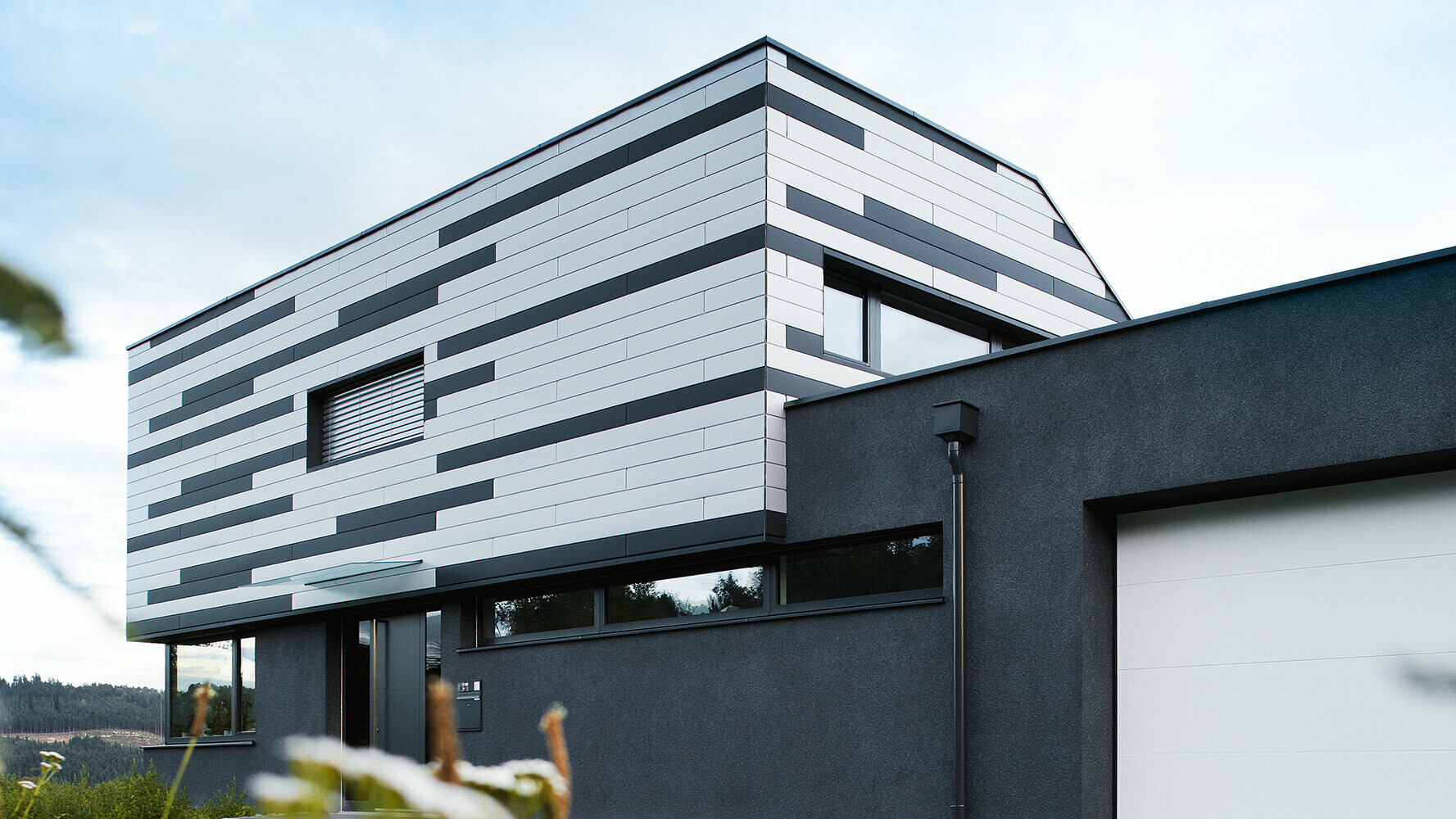 Moderní rodinný dům s kreativně ztvárněnou fasádou; systém PREFA Sidings byl položen střídavě ve stříbrné a antracitové barvě.