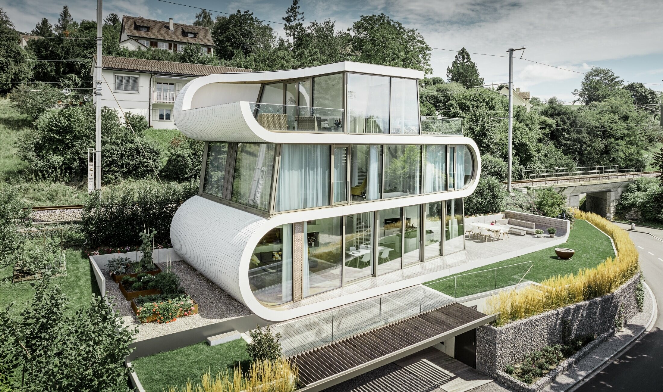 Velmi moderní rodinný dům navržený architektem Camenzindem z Curychu; Zakřivený pás spojuje jednotlivé úrovně navzájem. Křivky byly pokryty věžovkou PREFA v barvě čistě bílé. Díky velkým proskleným plochám působí celý dům velmi otevřeně. 